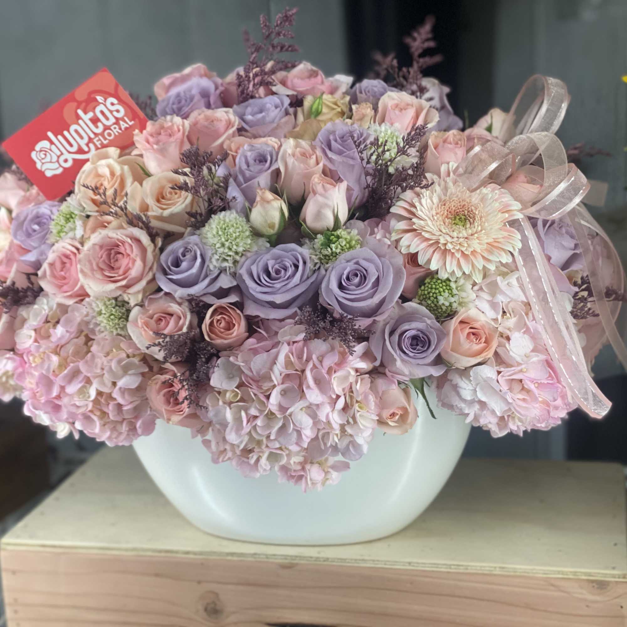 Pastel rose bouquet in a white vase with a ribbon bow
