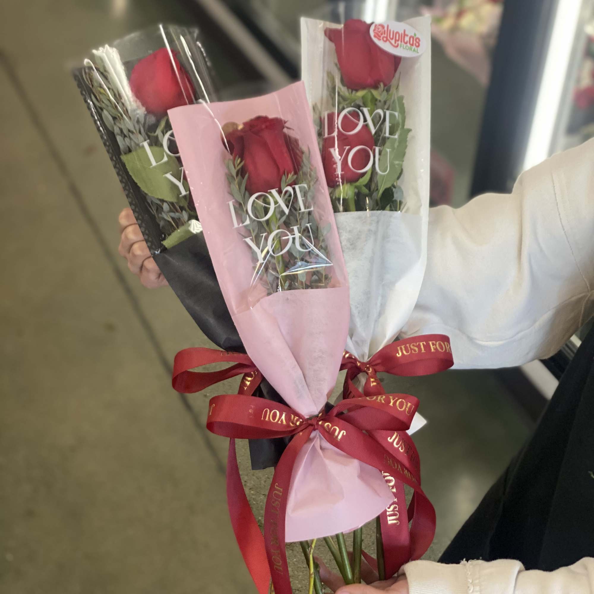 Three wrapped red rose bouquets with ribbons and "LOVE YOU" sleeves