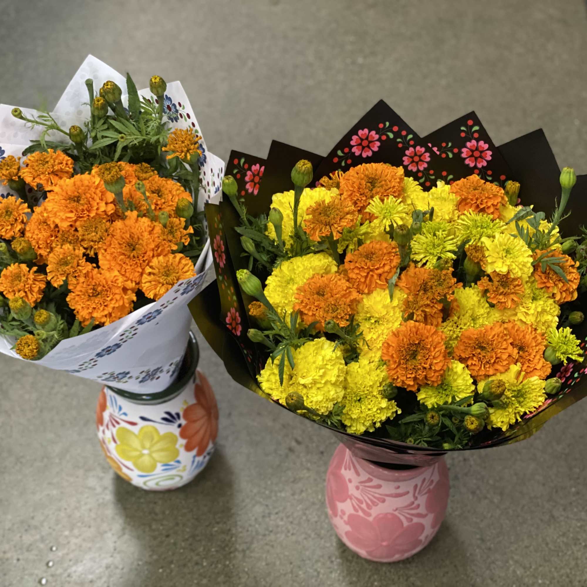Two marigold bouquets in painted ceramic vases on a concrete floor