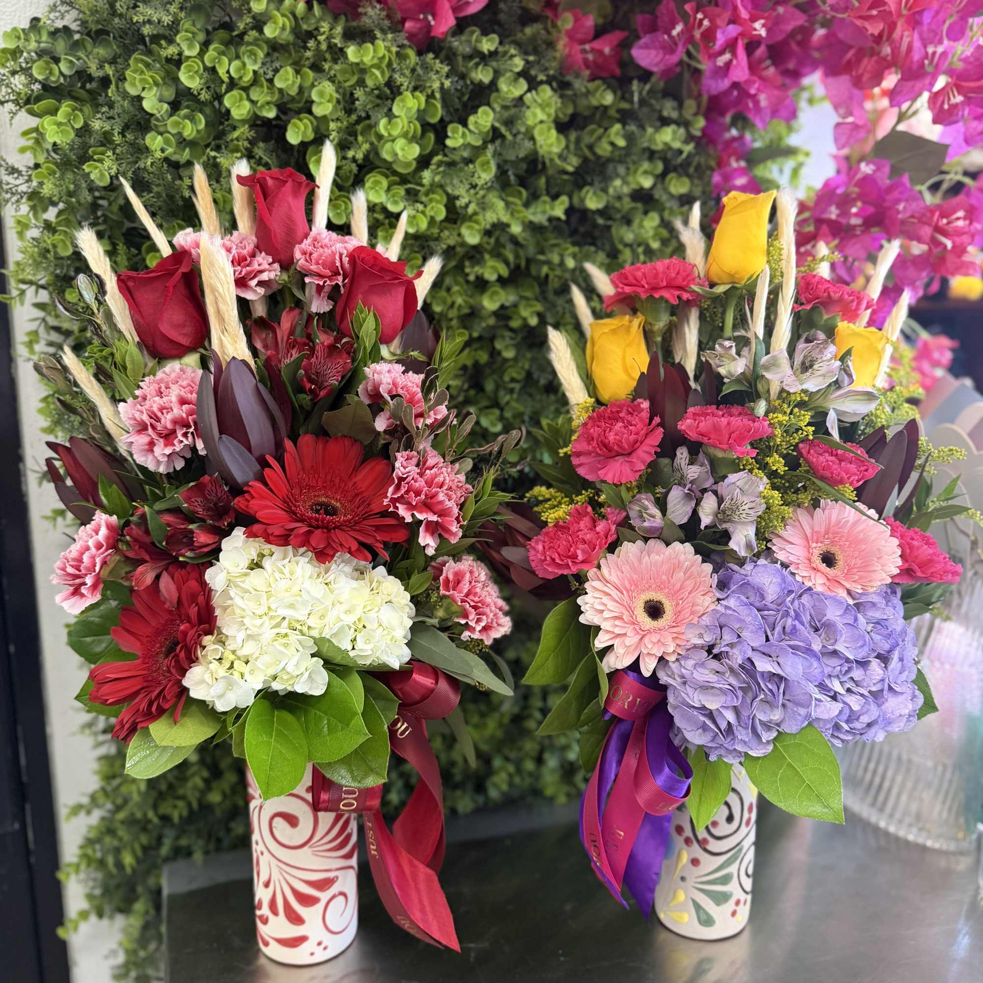 Two colorful floral arrangements in patterned vases with ribbons