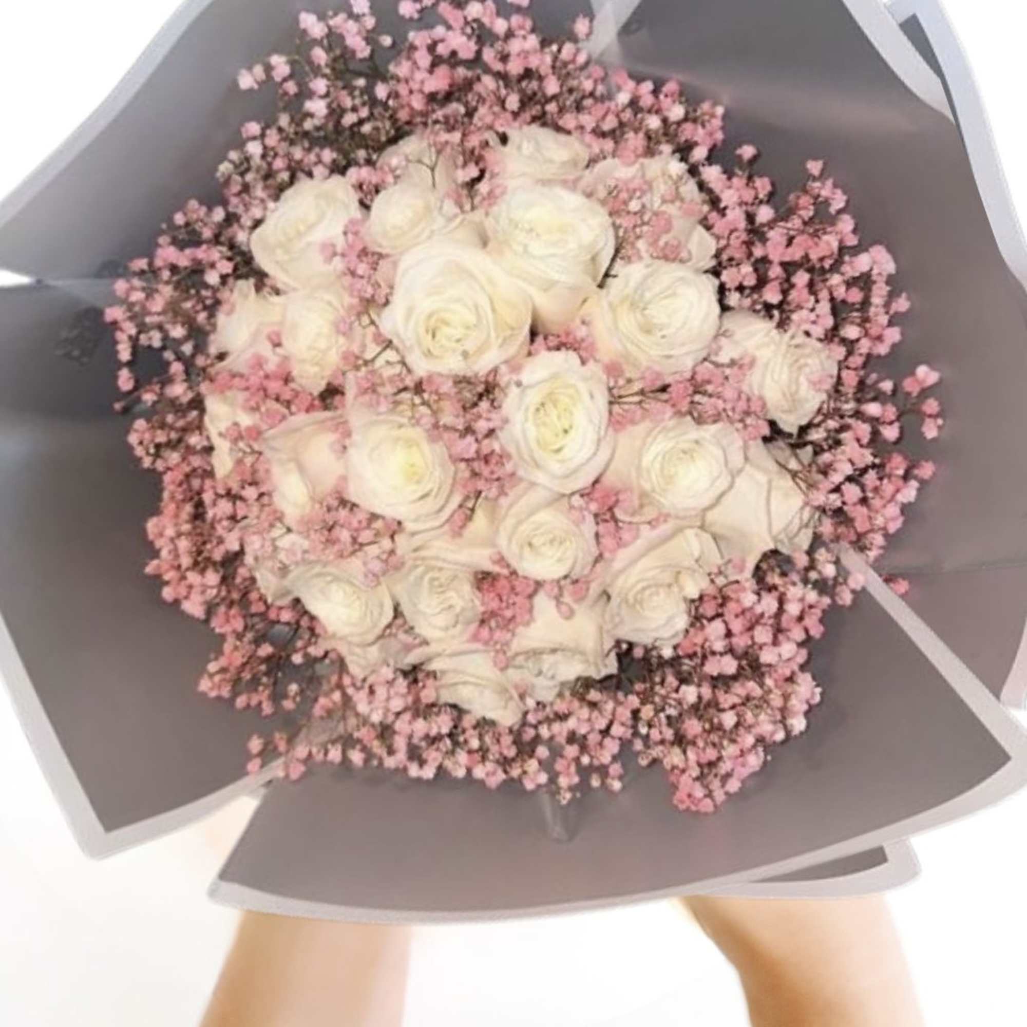 Bouquet of white roses with pink filler flowers in gray wrapping