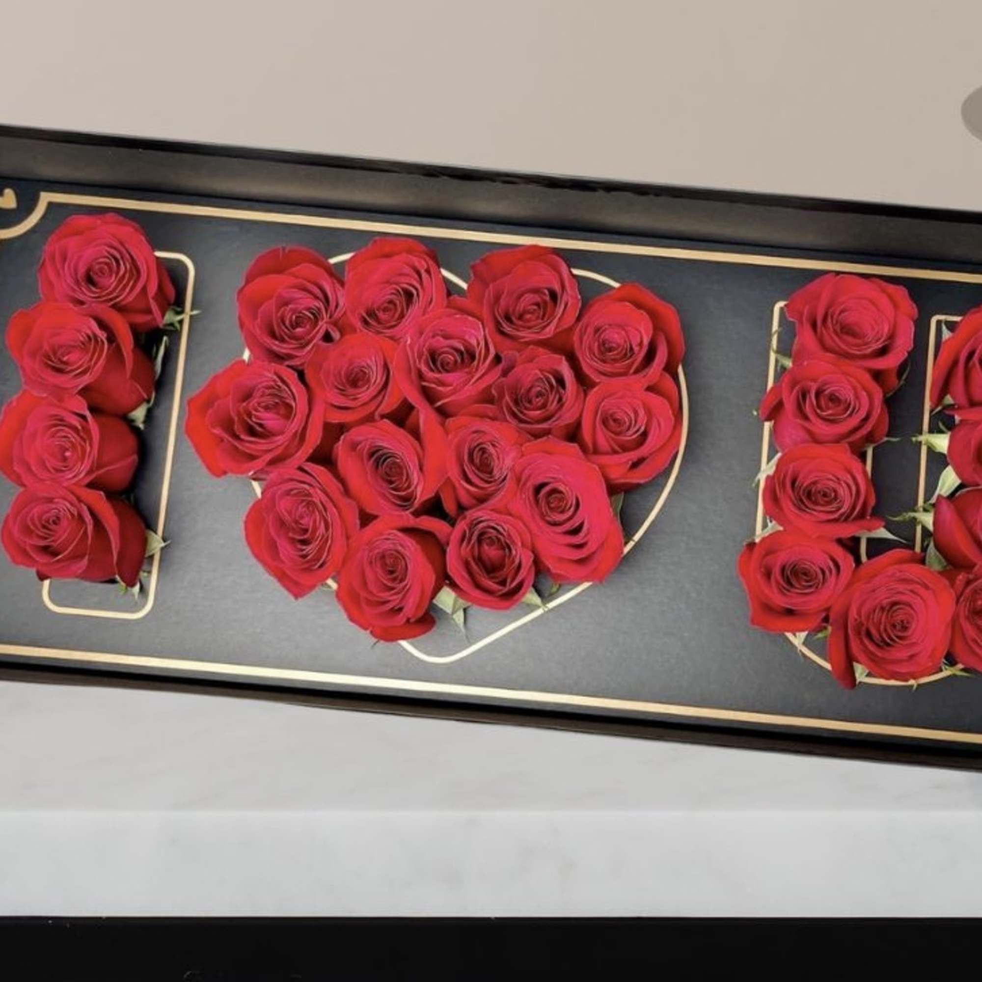 Red roses arranged to spell "I LOVE U" in a black tray