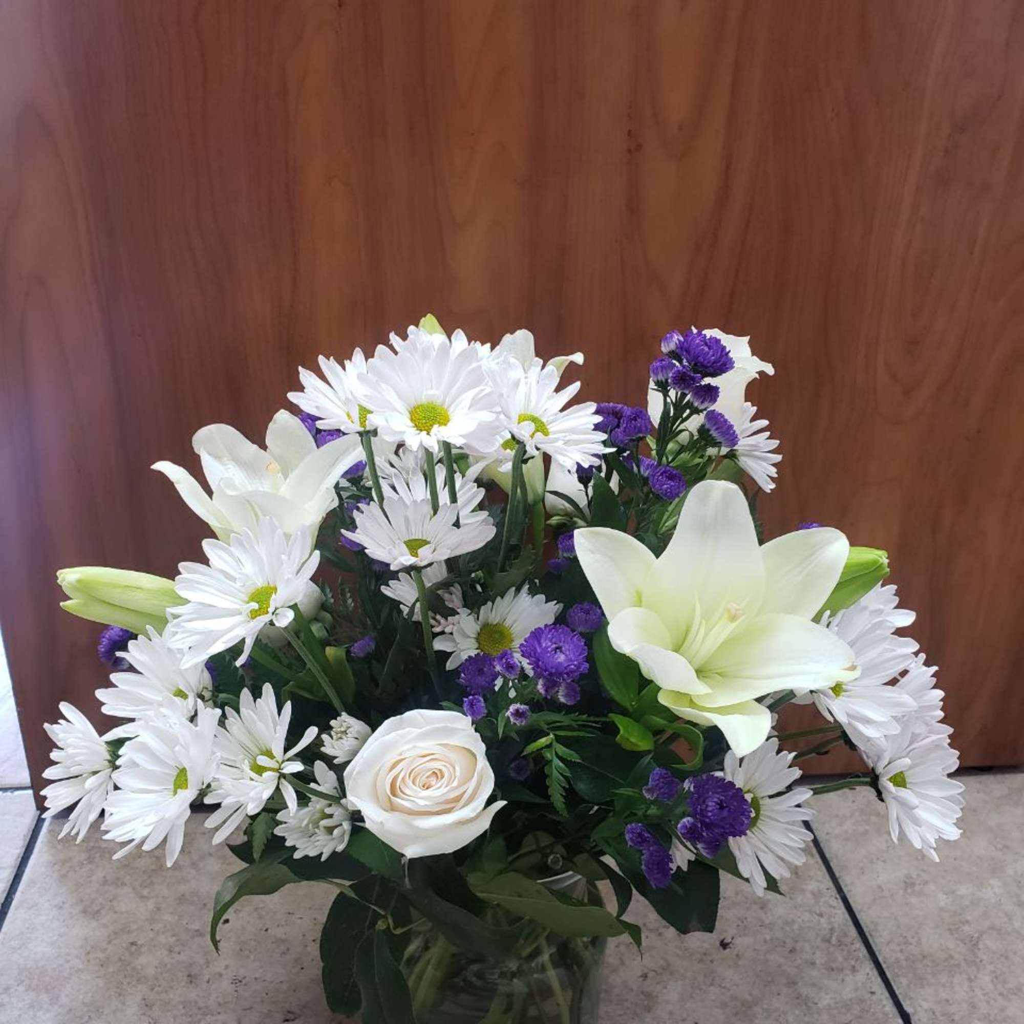 White daisies, lilies, and a rose in a glass vase