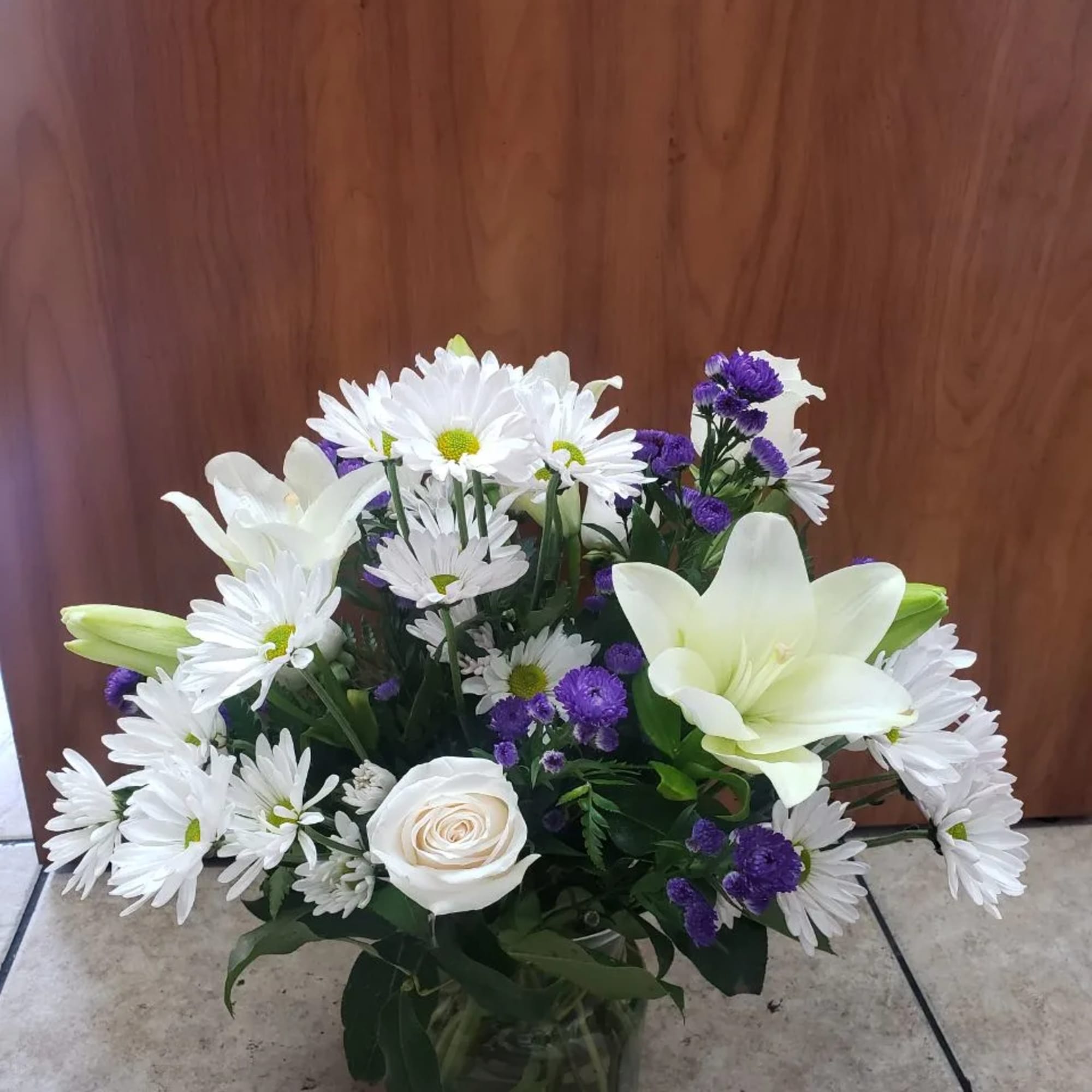 White daisies and lilies in a glass vase with purple filler flowers