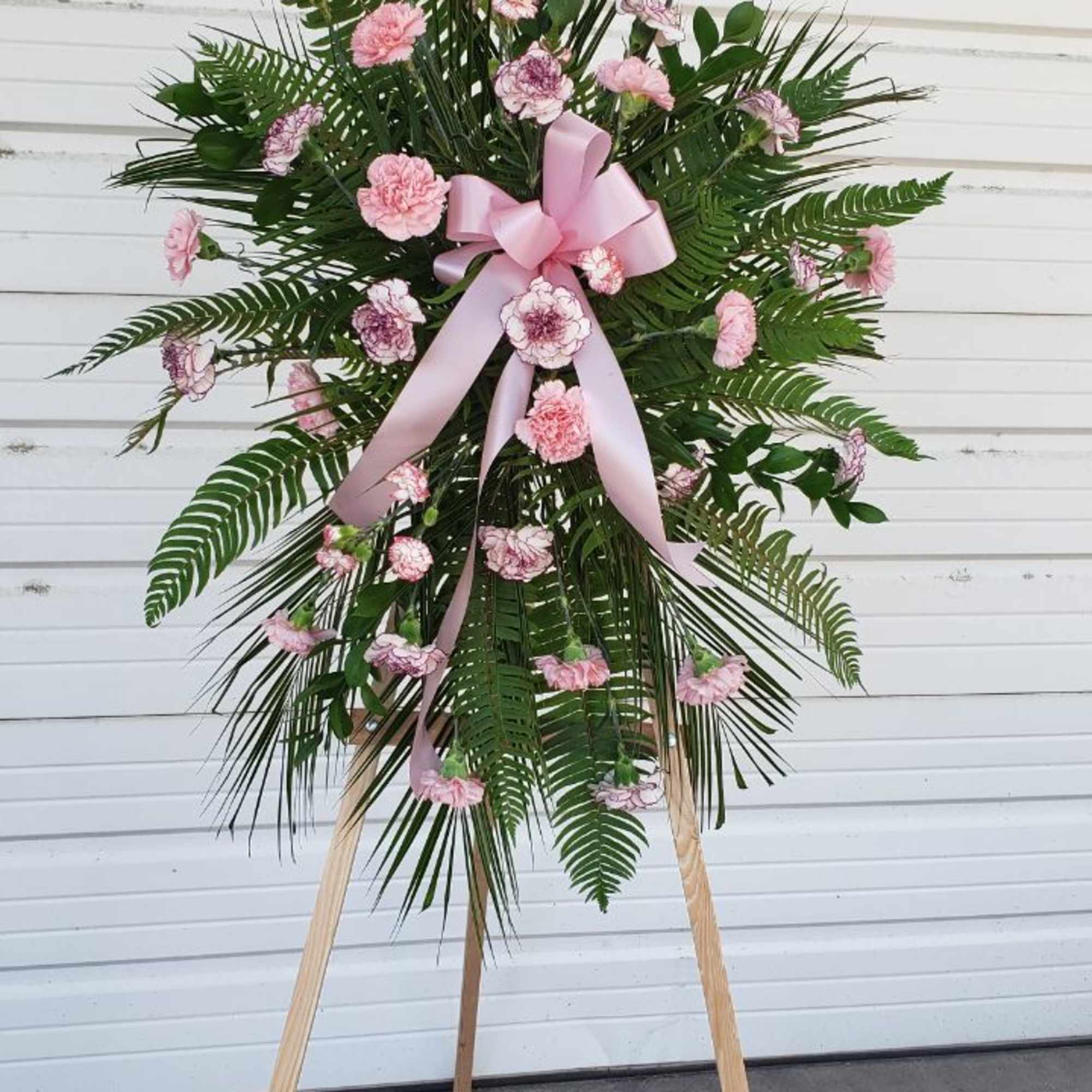 Standing floral spray with pink carnations and a pink ribbon on an easel