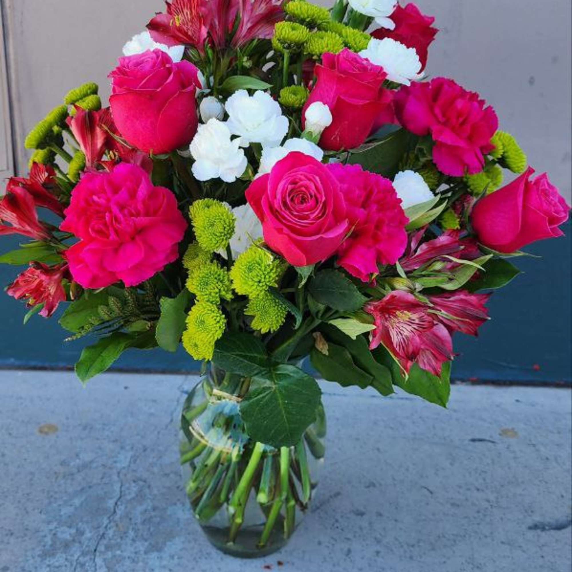 Bouquet of pink roses, white blooms, and green button mums in a glass vase