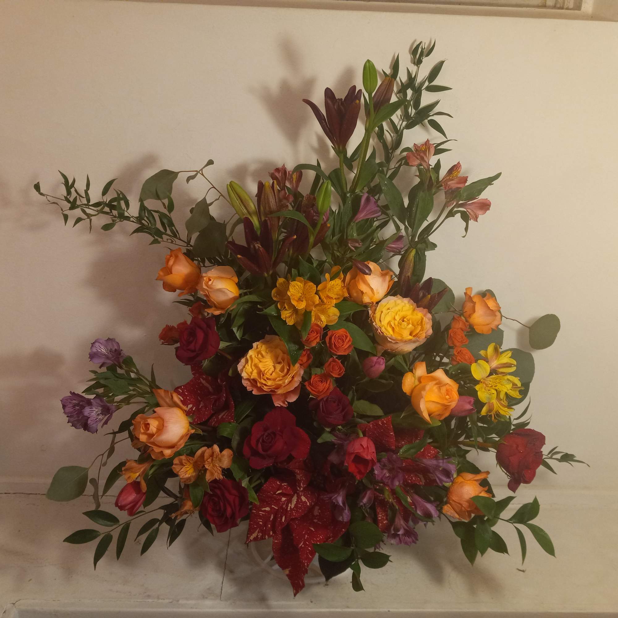 Mixed bouquet of roses and lilies in warm orange, red, and purple tones