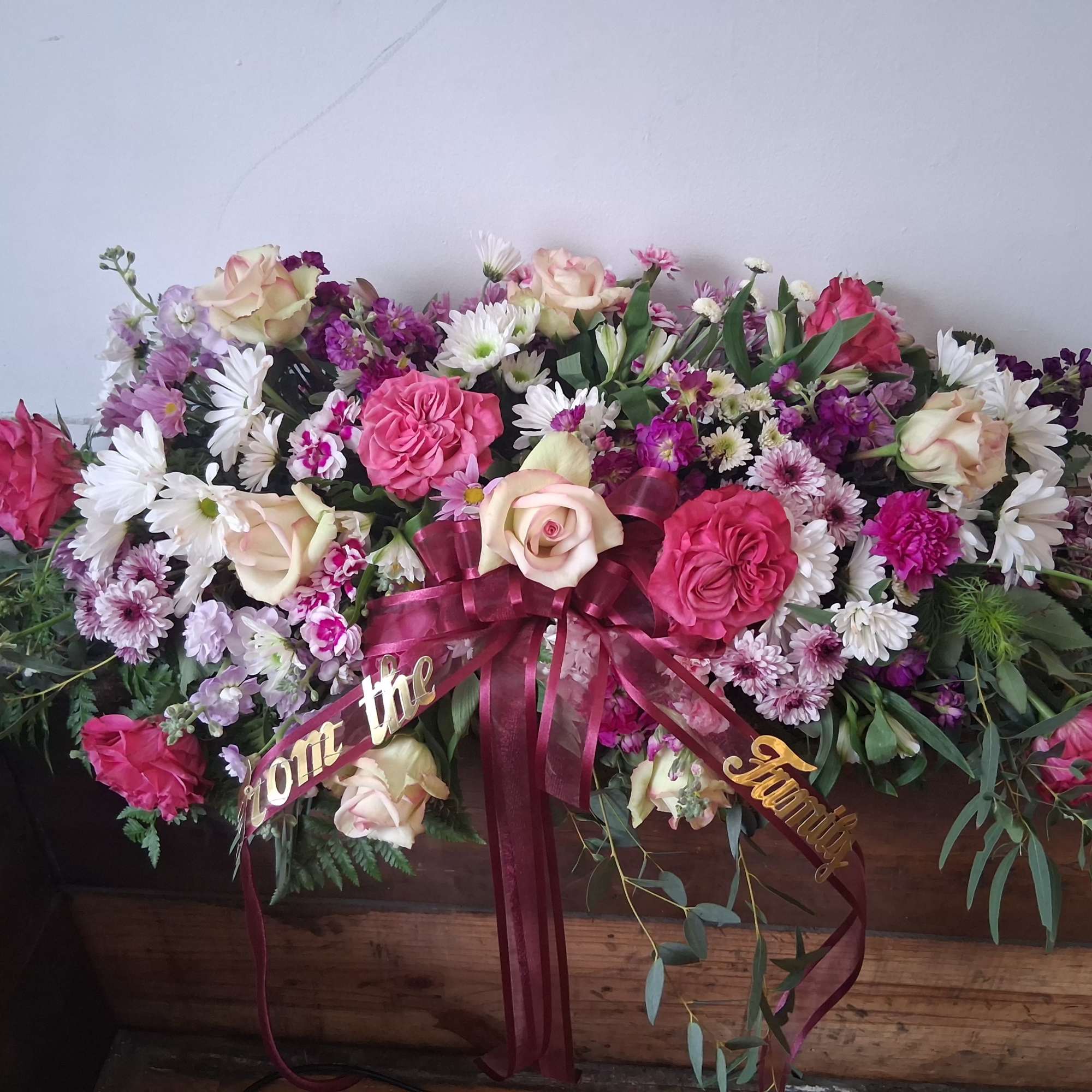 Large pink and white floral spray with ribbon on a casket