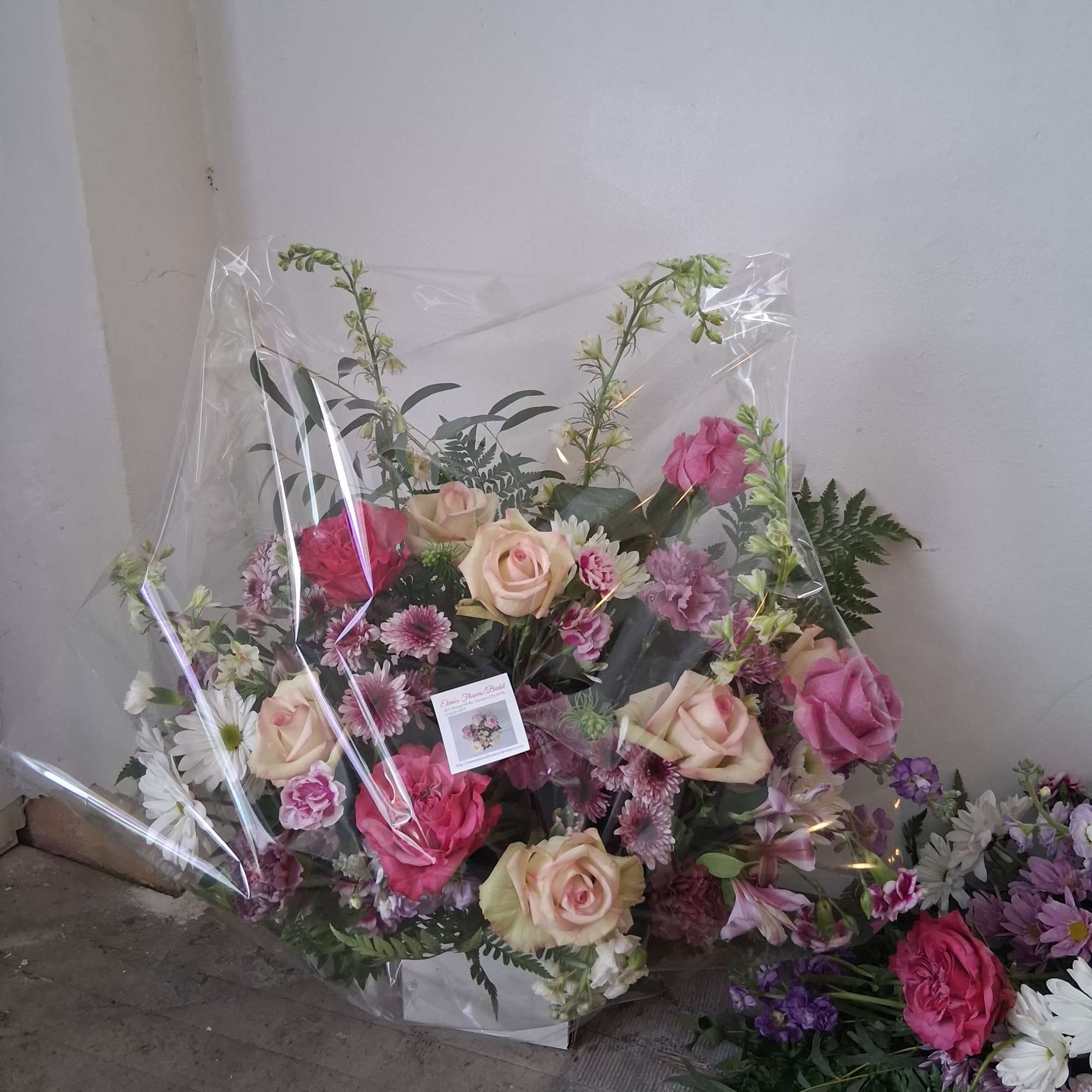 Mixed bouquet of roses, daisies, and pink blooms wrapped in clear plastic