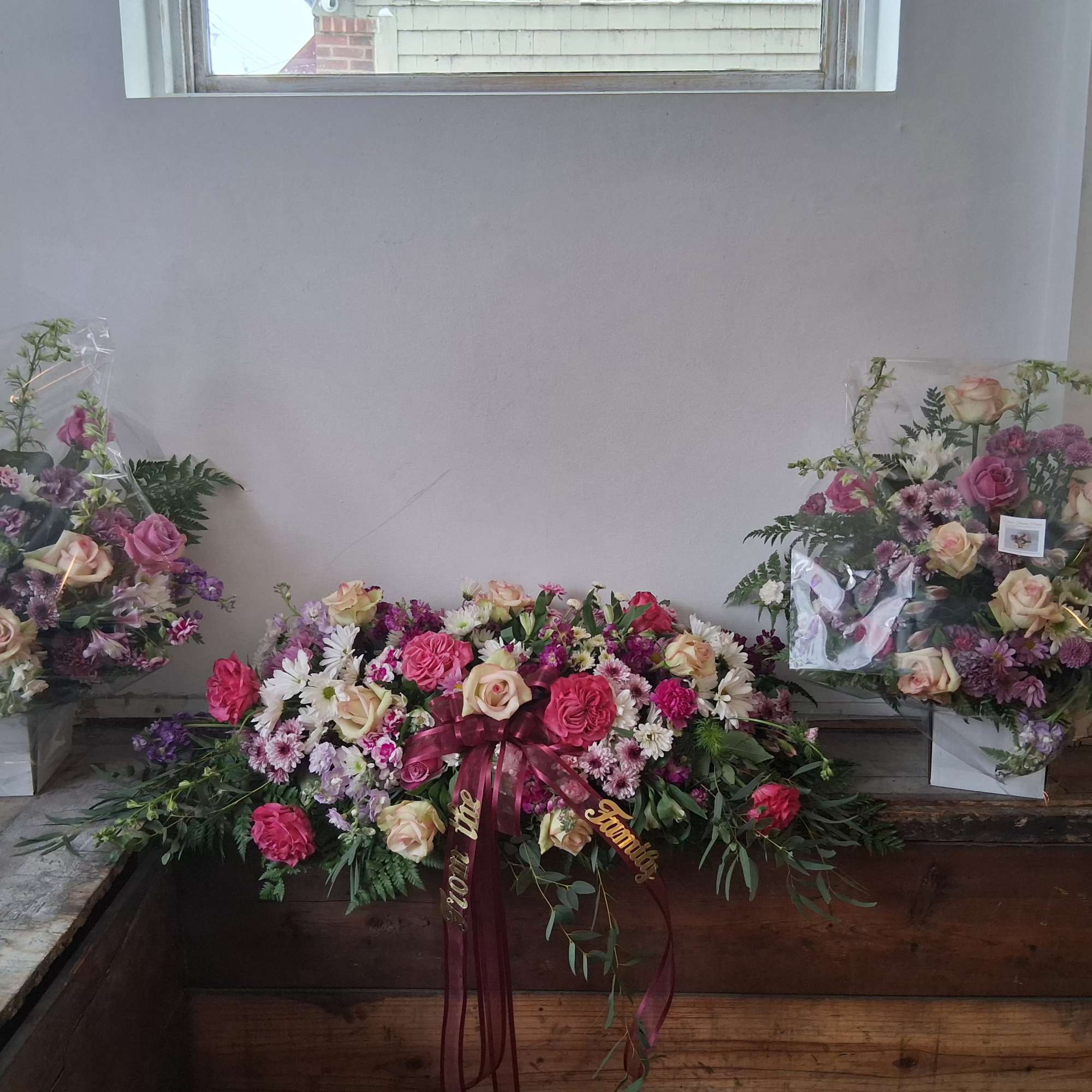 Three floral arrangements with pink and cream roses and daisies, two in boxes and one low centerpiece.