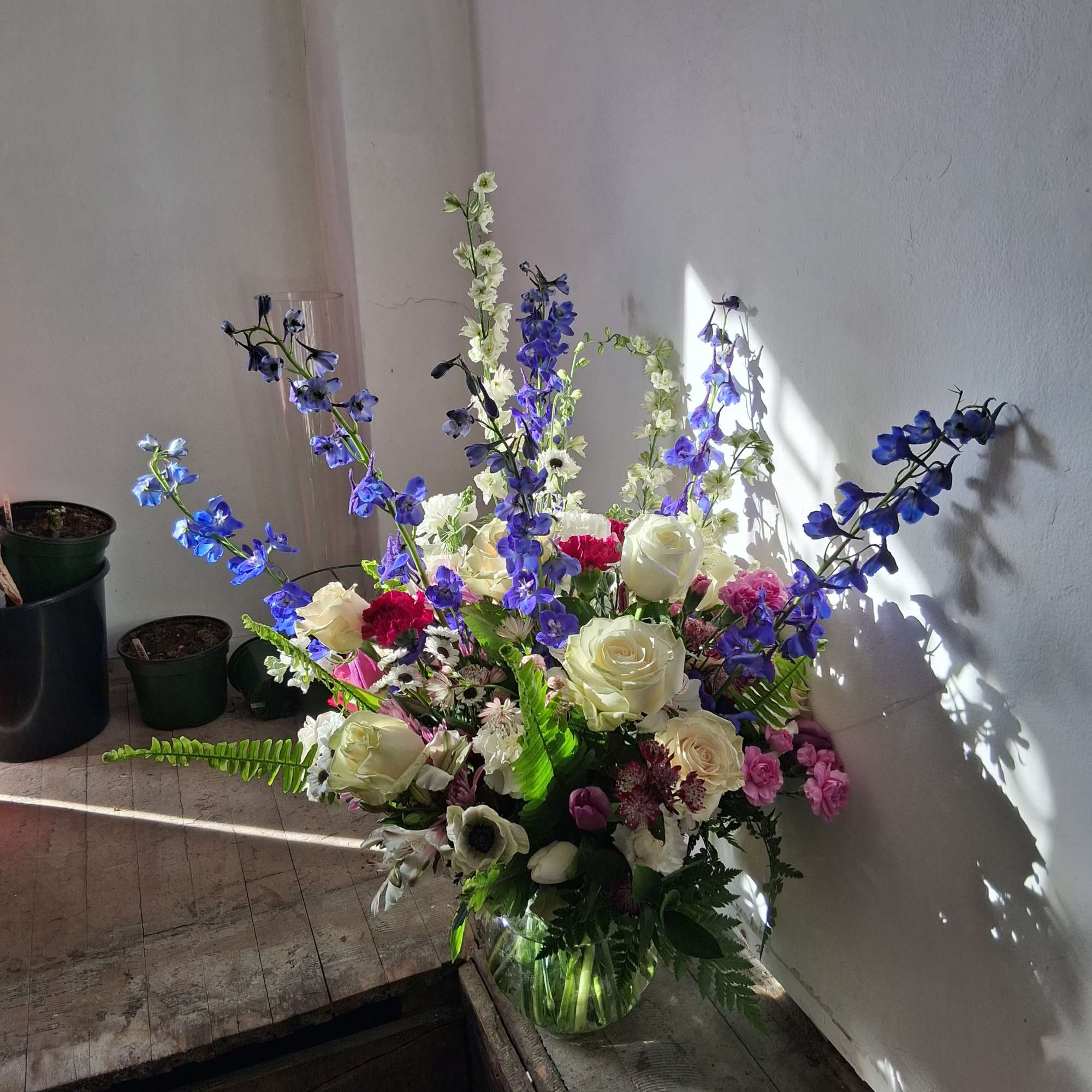 Tall mixed bouquet of white roses, blue delphinium, and pink flowers in a glass vase
