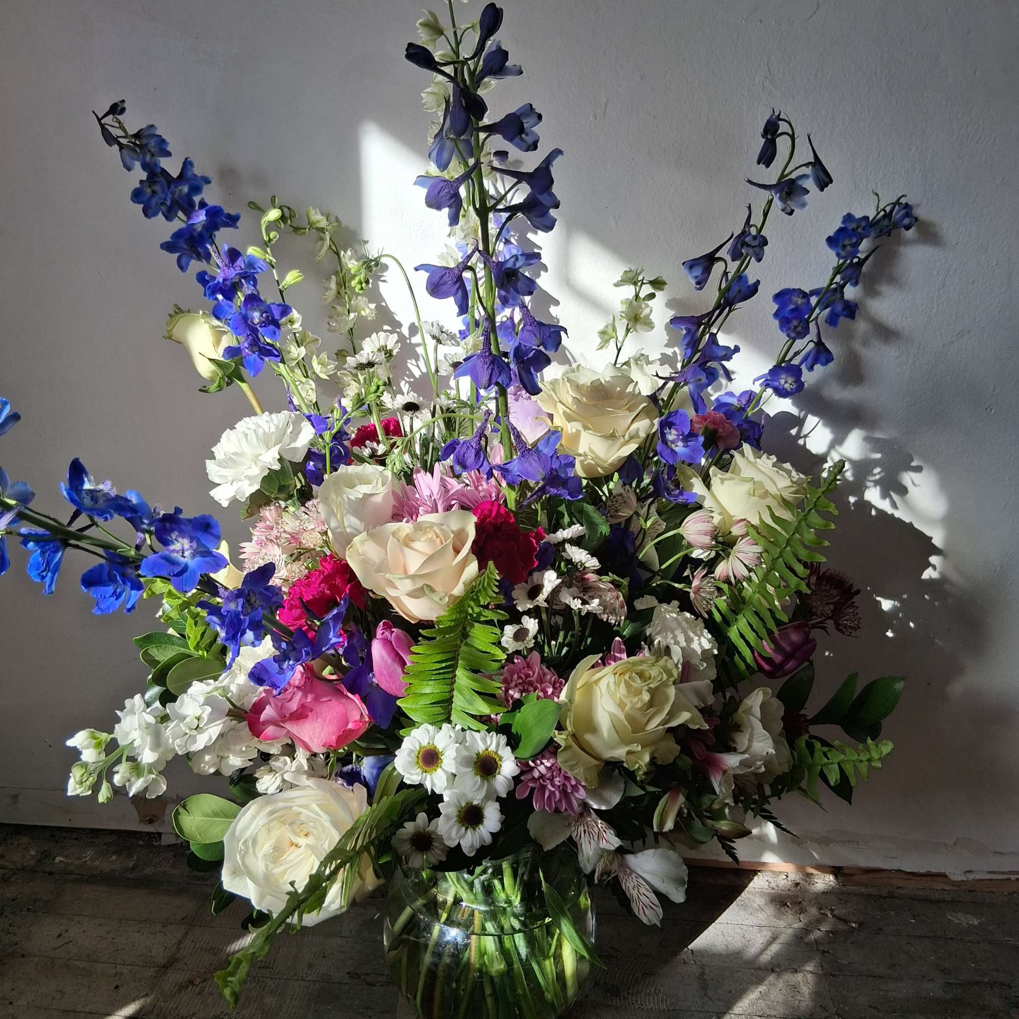 Large mixed bouquet in a glass vase with blue delphinium and cream roses