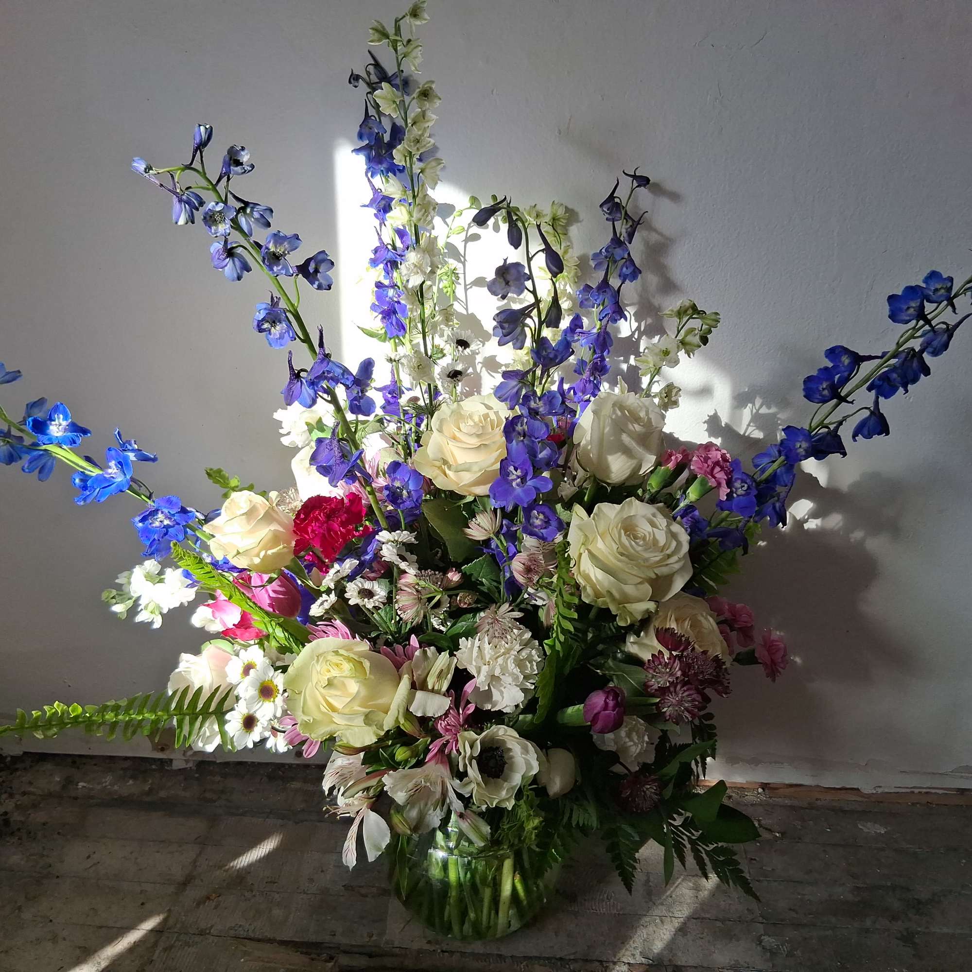 Tall mixed bouquet in a glass vase with blue delphinium and white roses