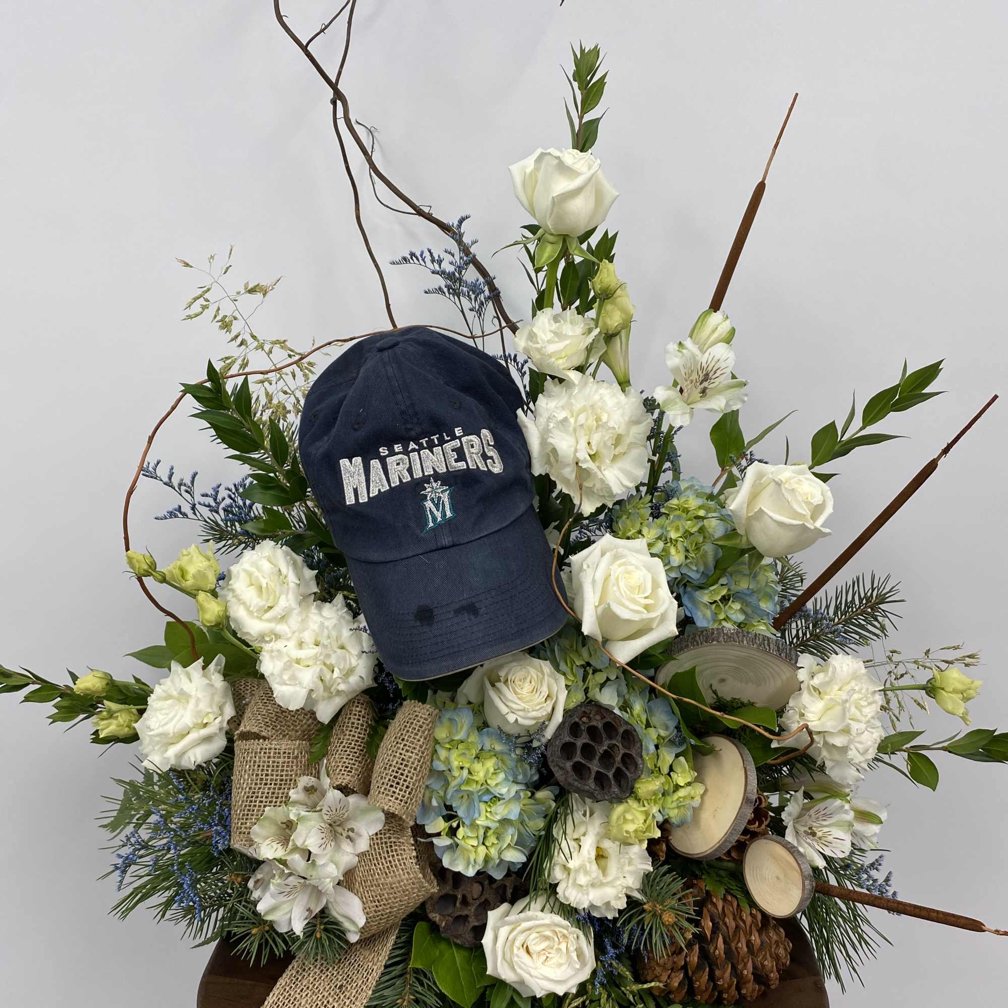 Floral arrangement with white roses, hydrangeas, and a Seattle Mariners cap
