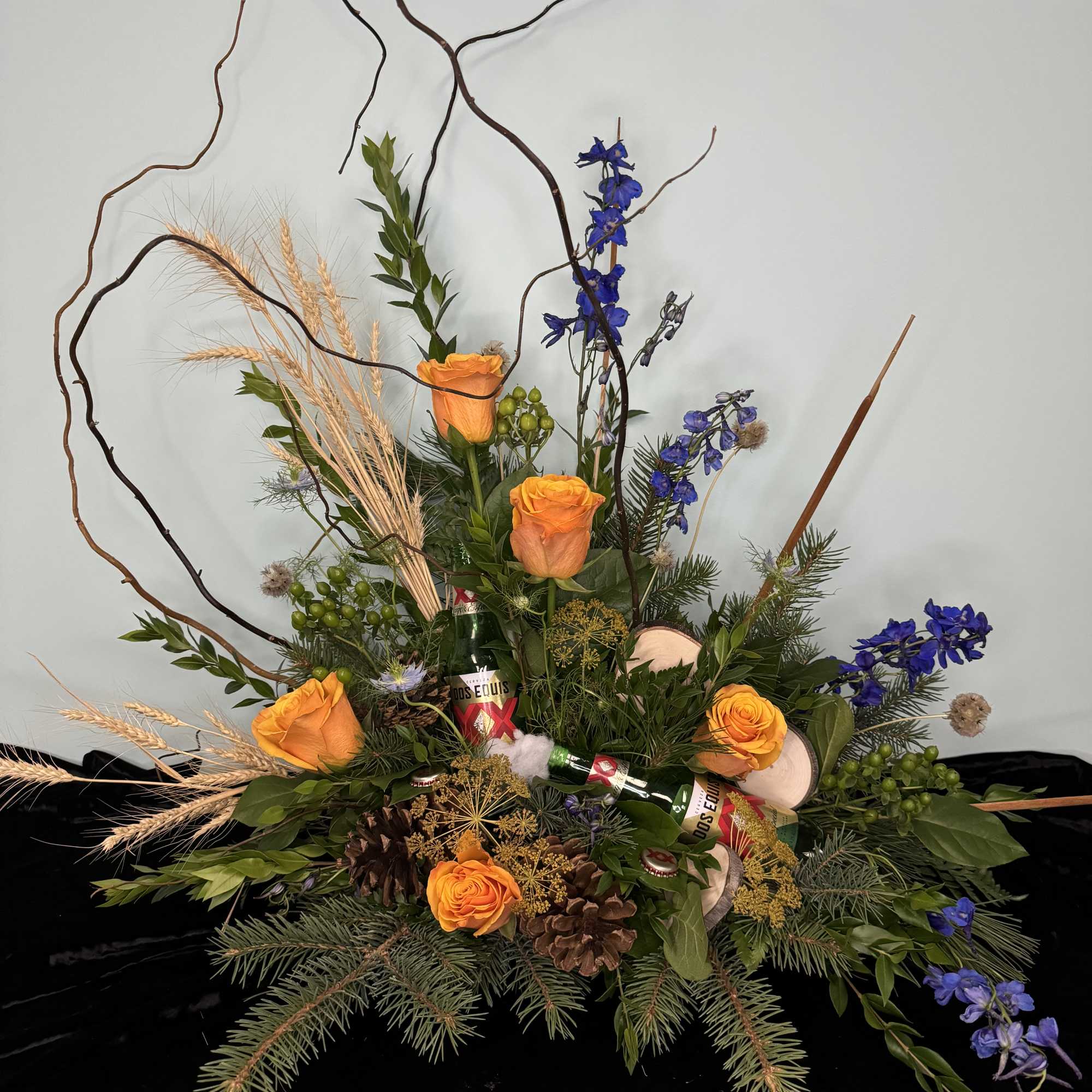 Tall floral arrangement with orange roses and blue flowers in a low base