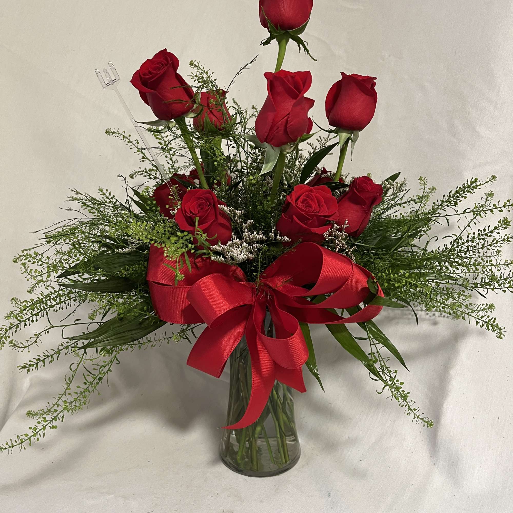 Red roses arranged in a clear glass vase with a large red ribbon