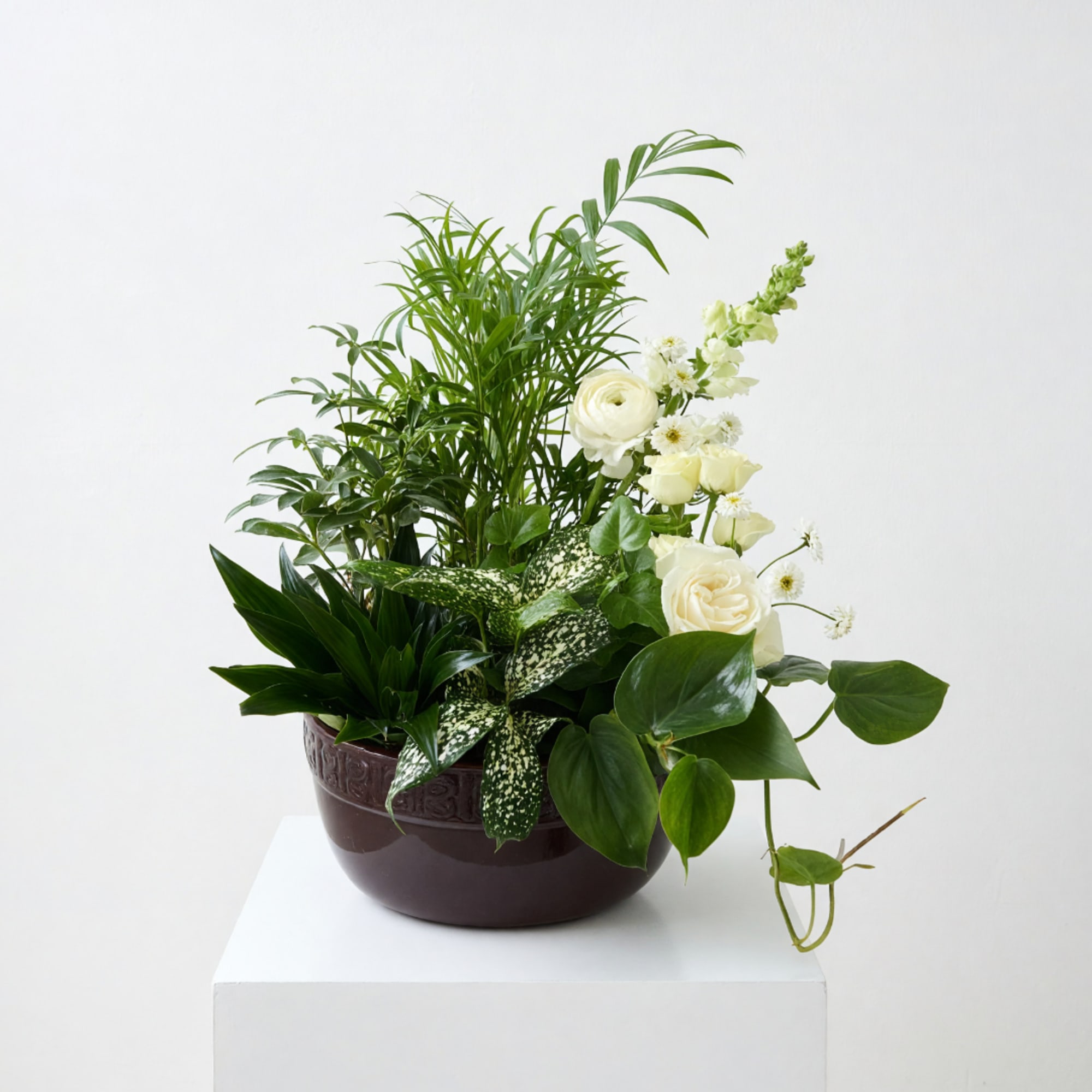 White roses and mixed greenery arranged in a brown bowl vase