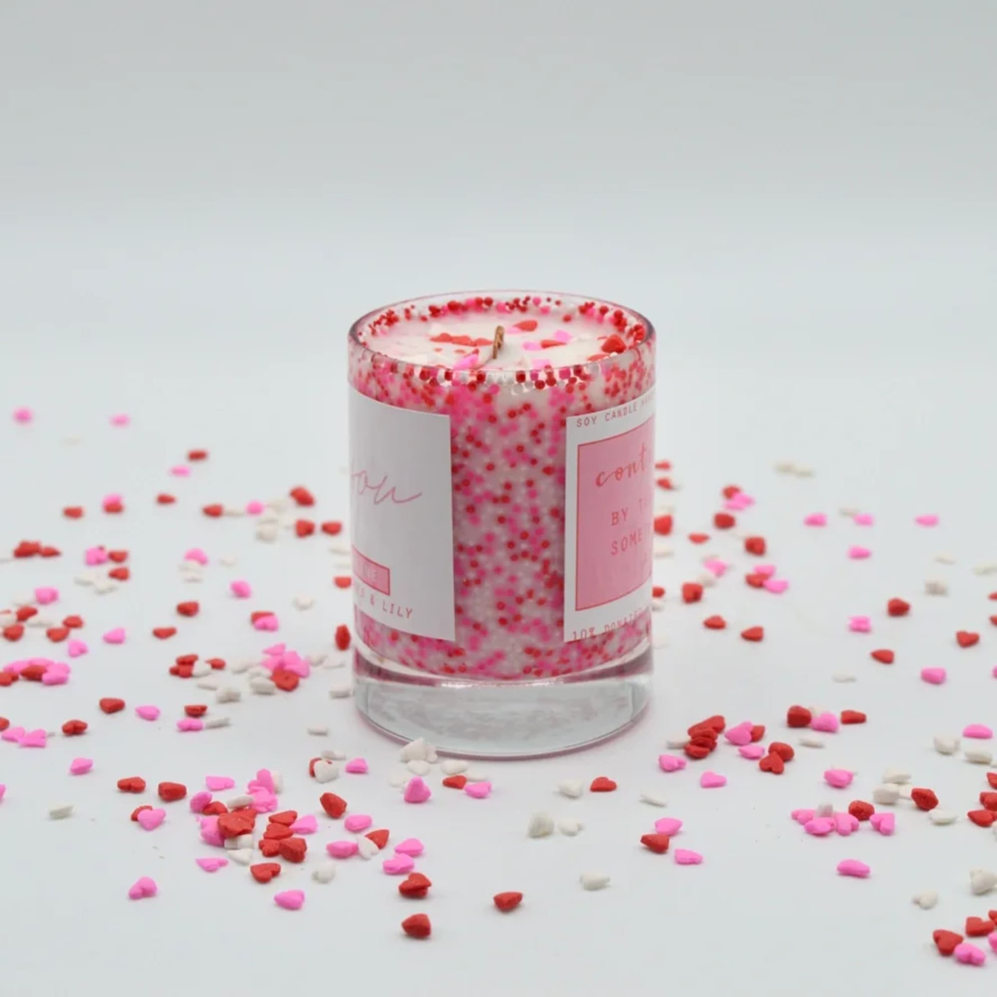 Pink and red soy candle in a glass jar with heart confetti around it