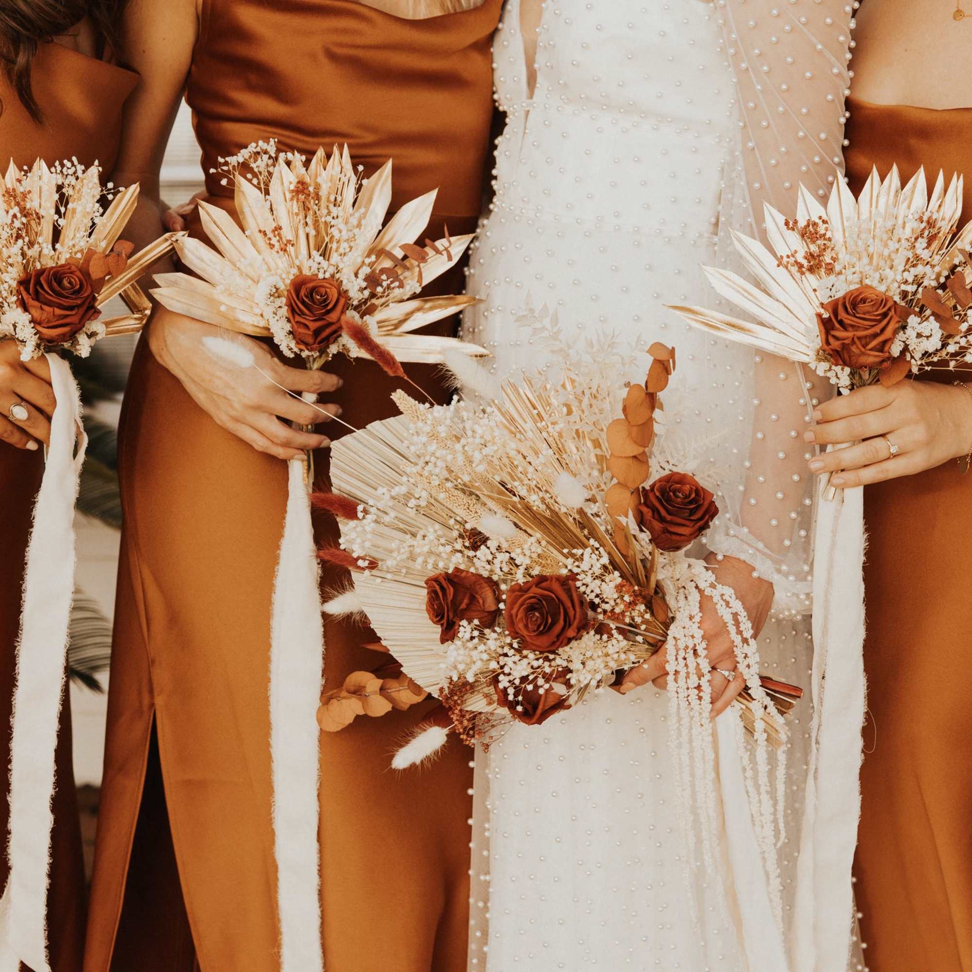 Bridesmaids hold rust-colored bouquets beside a bride in white.