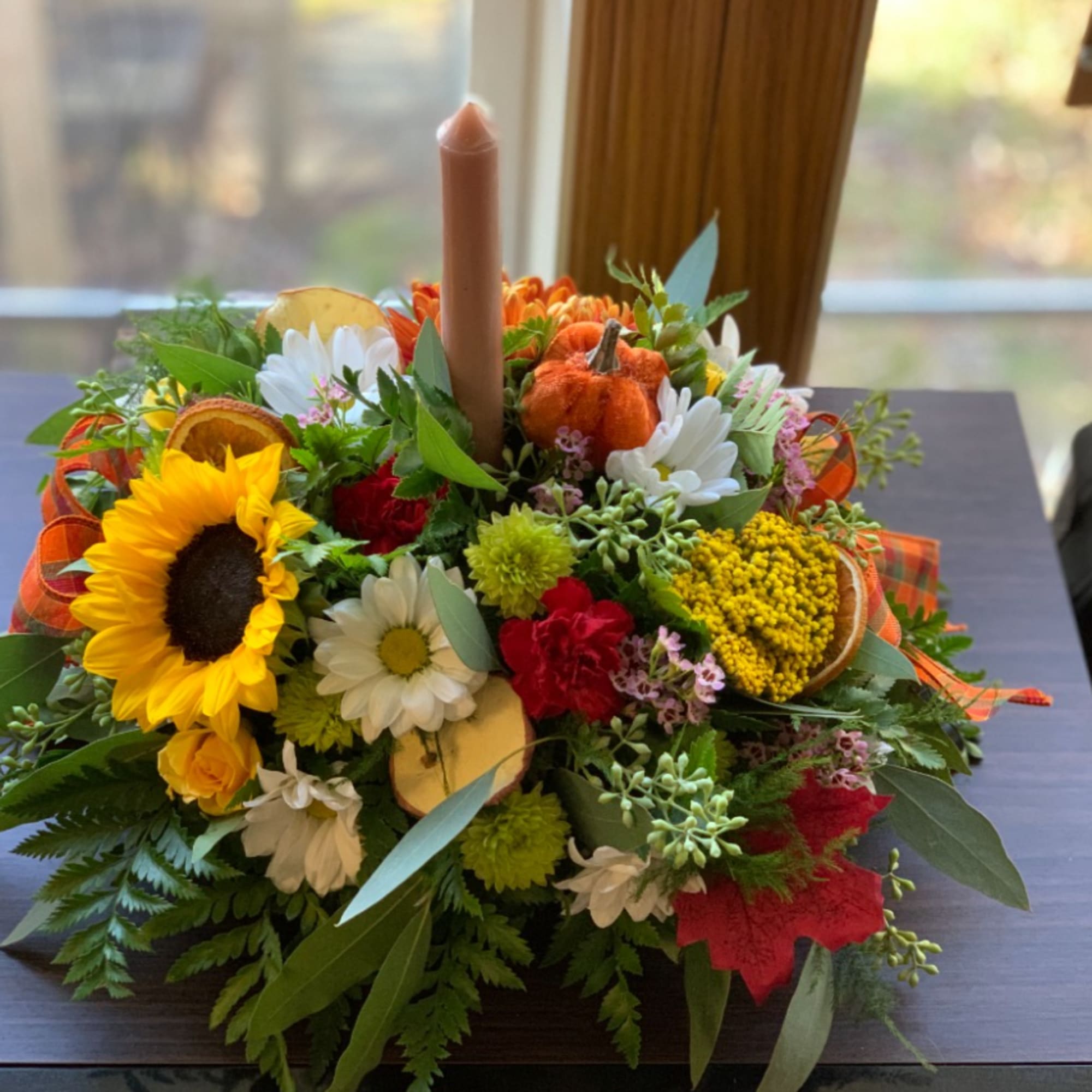 Autumn floral centerpiece with a candle, sunflowers, daisies, and small pumpkins