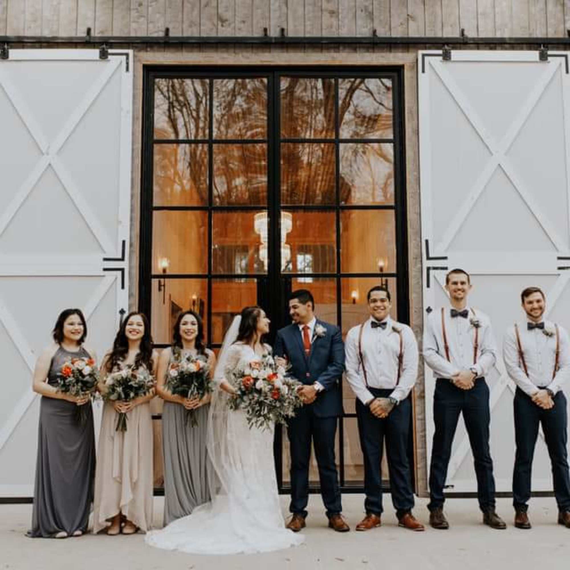 Wedding party posing outside a barn with bouquets and boutonnieres