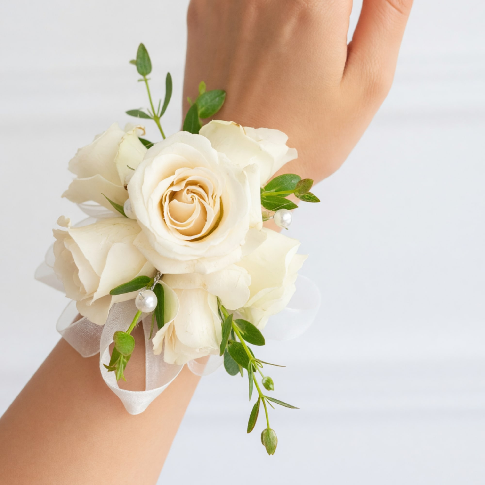 White rose wrist corsage with ribbon and greenery on a wrist