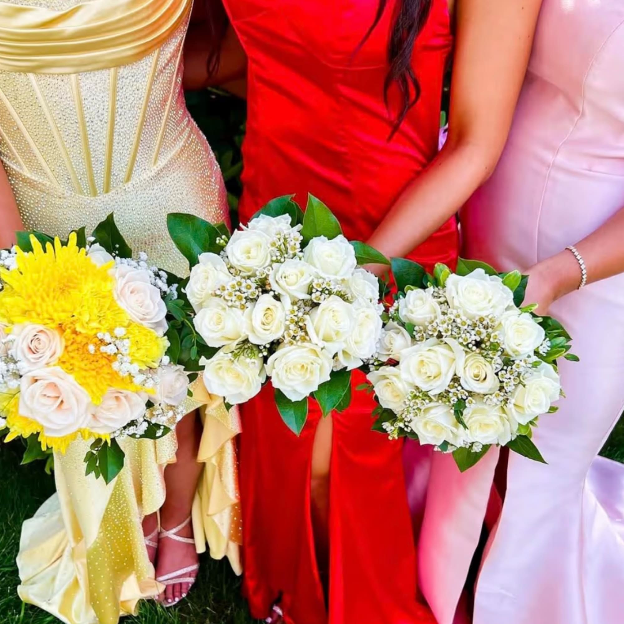 Three women hold bouquets of white and yellow roses in formal dresses.