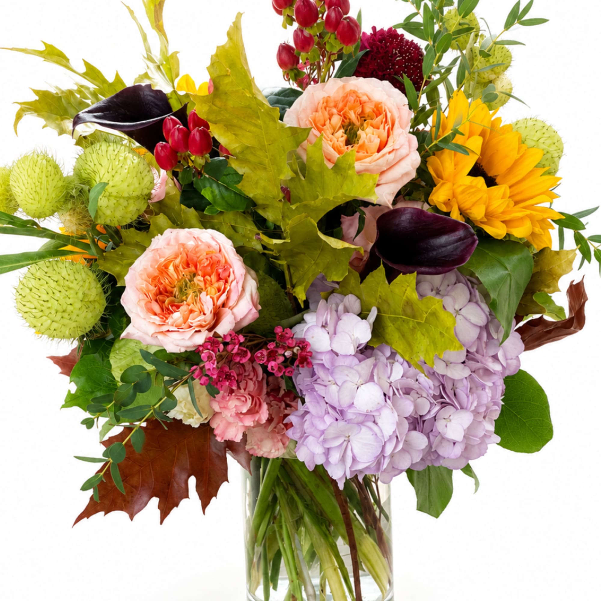 Mixed bouquet in a clear glass vase with hydrangeas, roses, sunflowers, and calla lilies