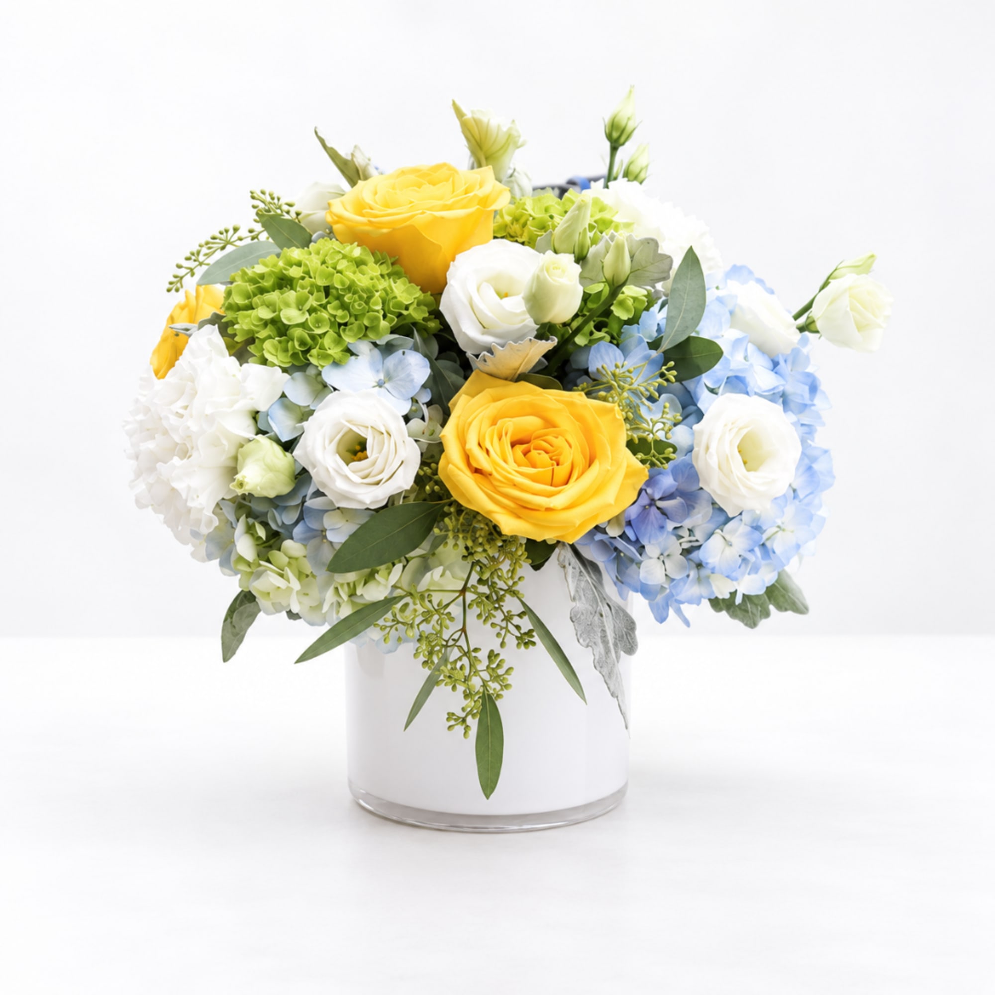 Yellow and white roses with blue hydrangeas in a clear glass vase