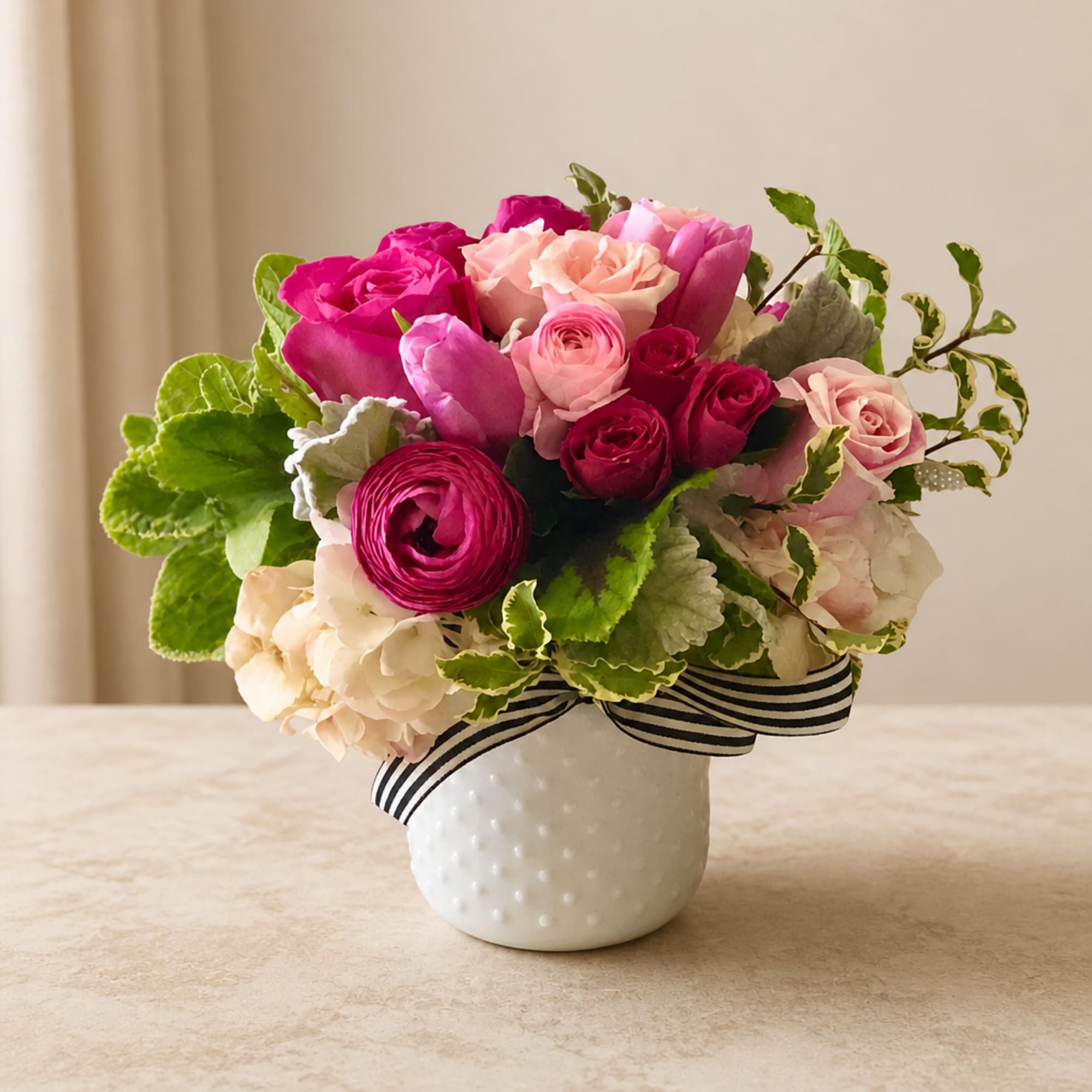 Pink and peach flower arrangement in a white vase with a striped ribbon