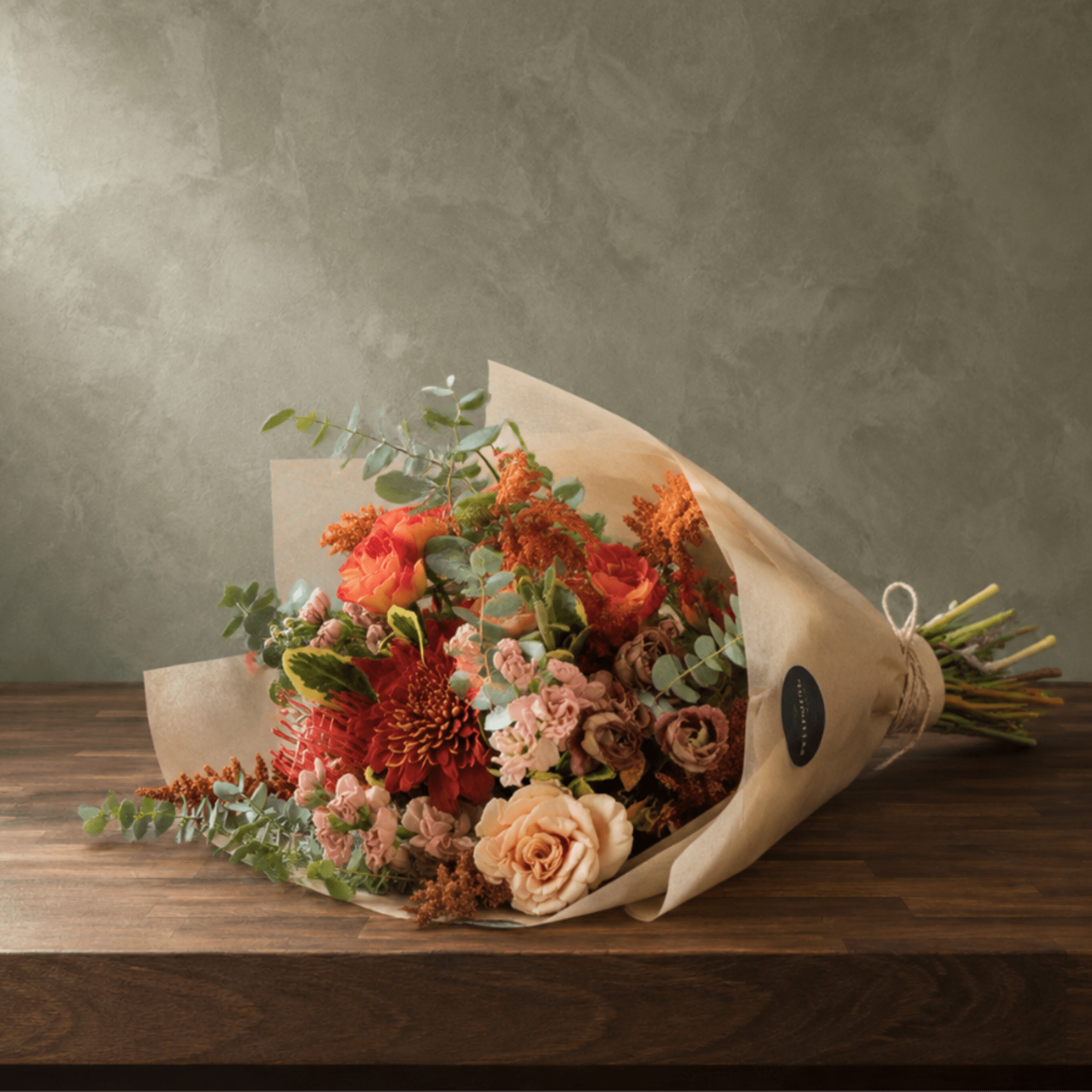 Bouquet of orange, peach, and pink flowers wrapped in kraft paper