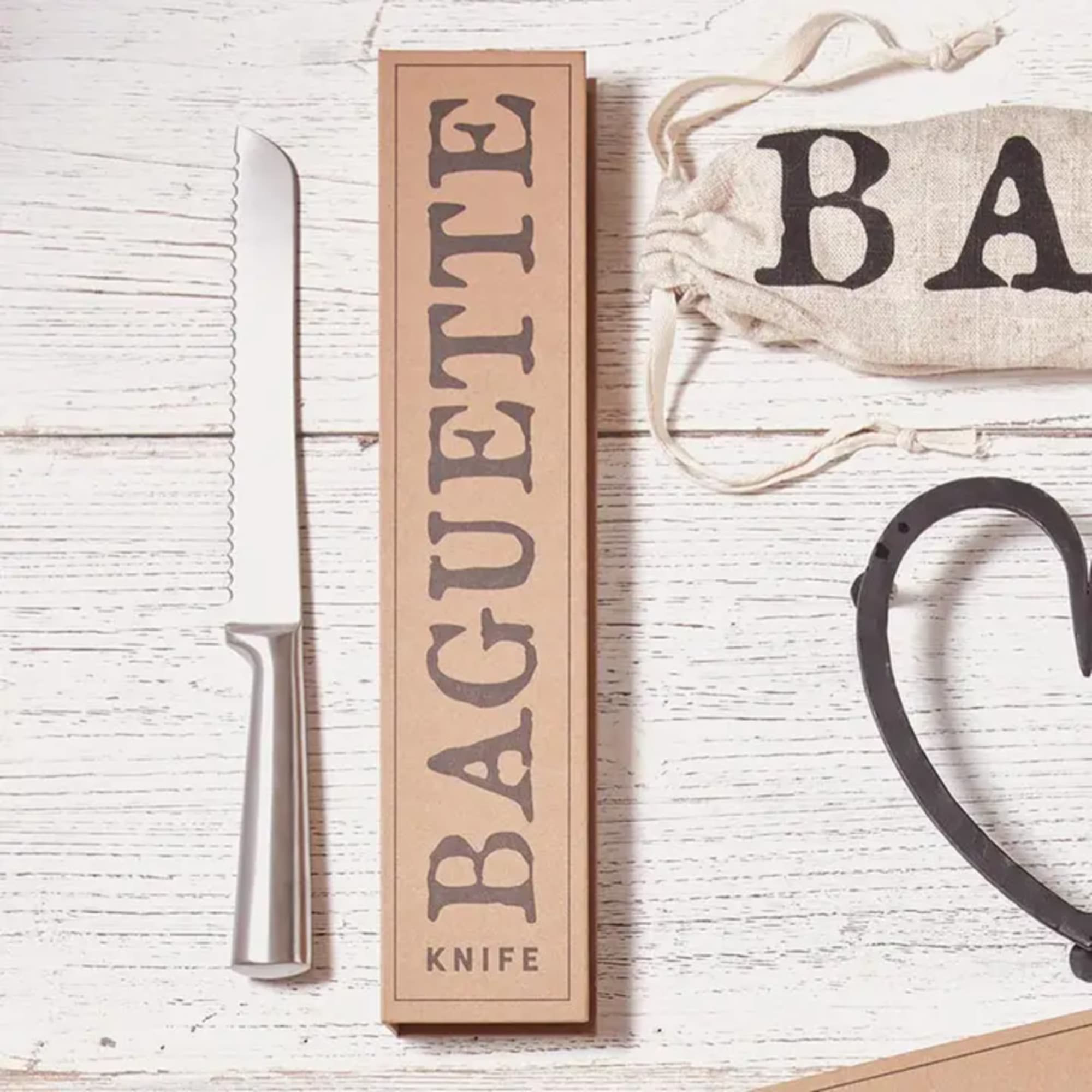 Bakery knife with packaging and a cloth bag on a white wooden surface