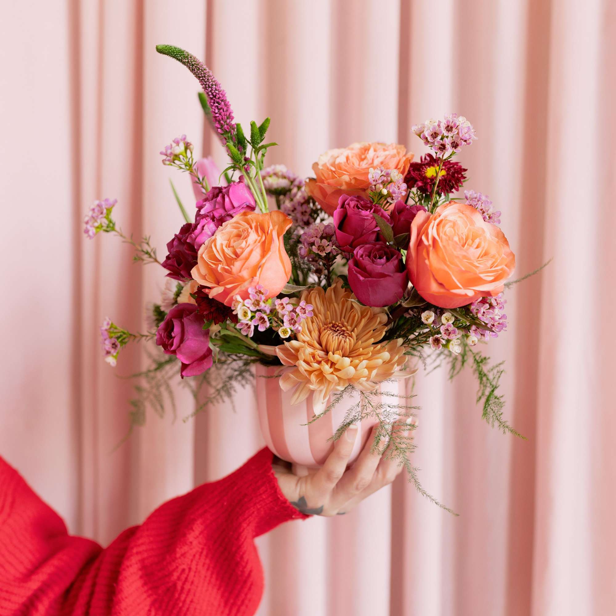 Handheld bouquet of peach and pink roses in a striped vase