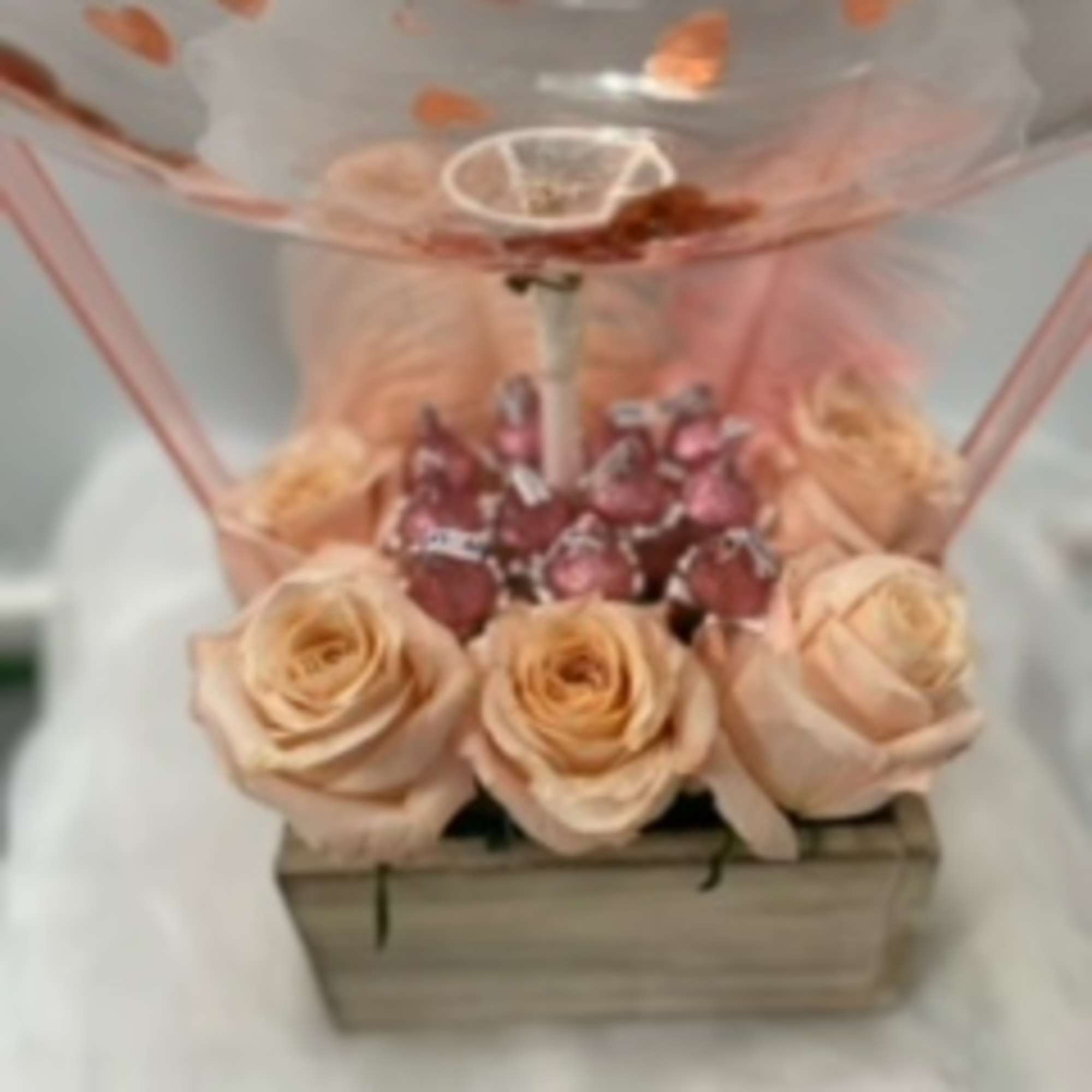 Peach roses arranged in a wooden box with a clear balloon above