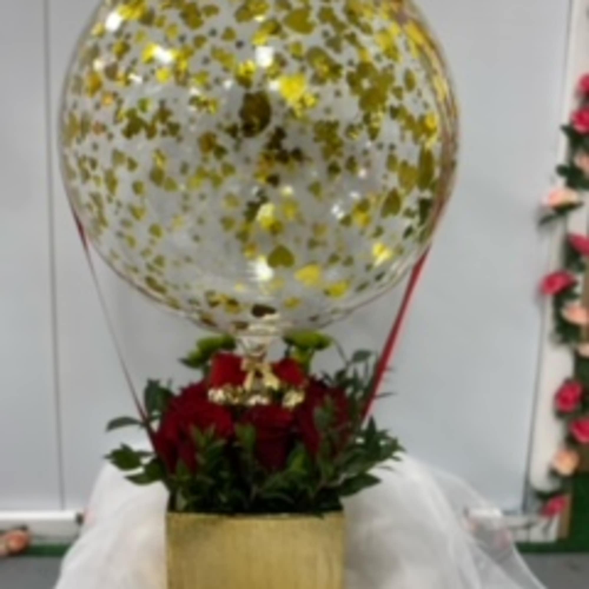 Gold confetti balloon above red roses in a square box