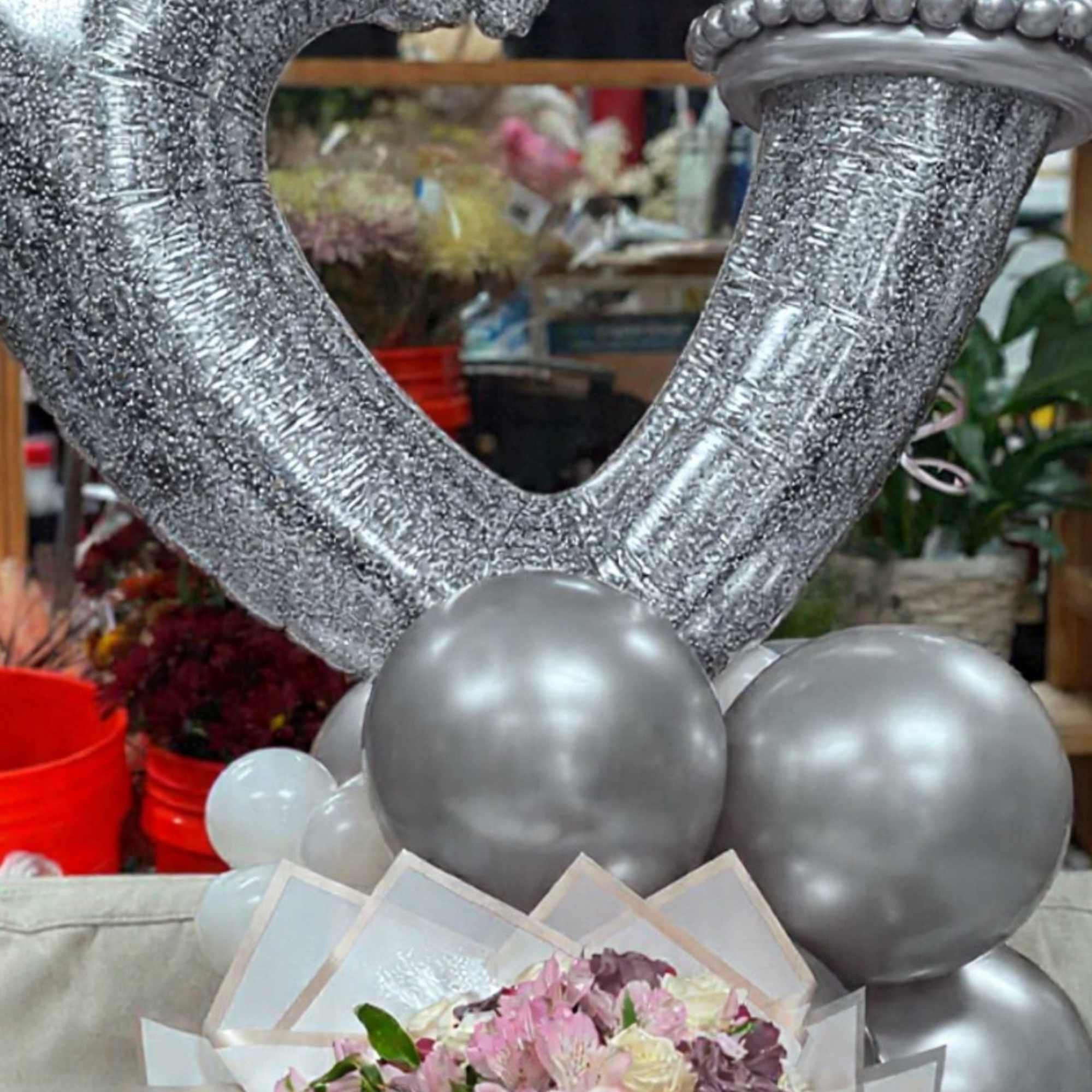 Silver heart-shaped balloons above a bouquet of pink and cream roses