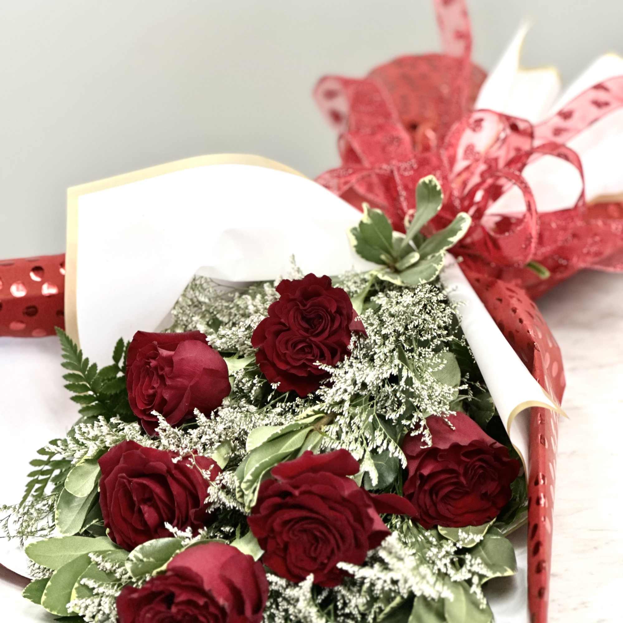 Bouquet of red roses wrapped in white paper with red ribbon