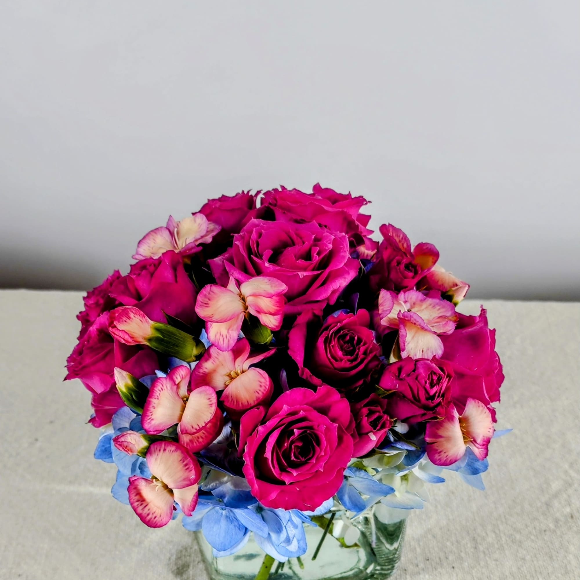 Pink rose bouquet in a square glass vase with blue flowers