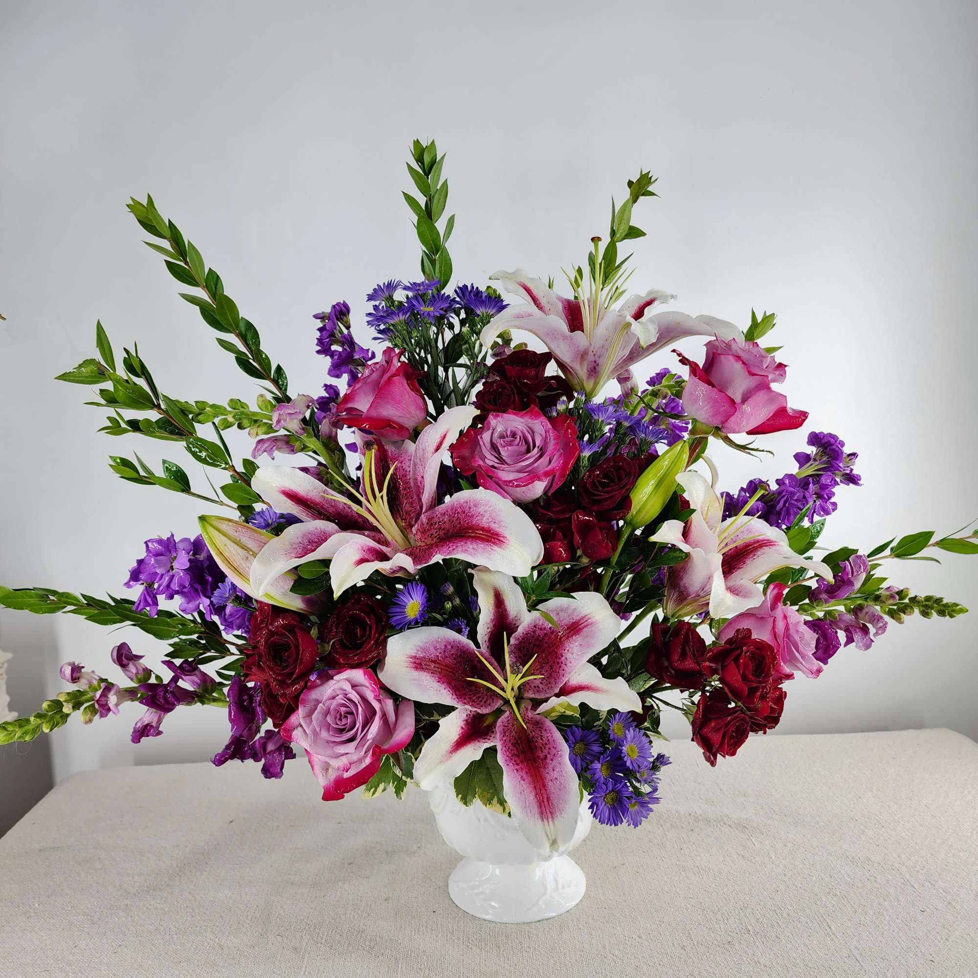 Mixed bouquet of pink roses, lilies, and purple flowers in a white vase