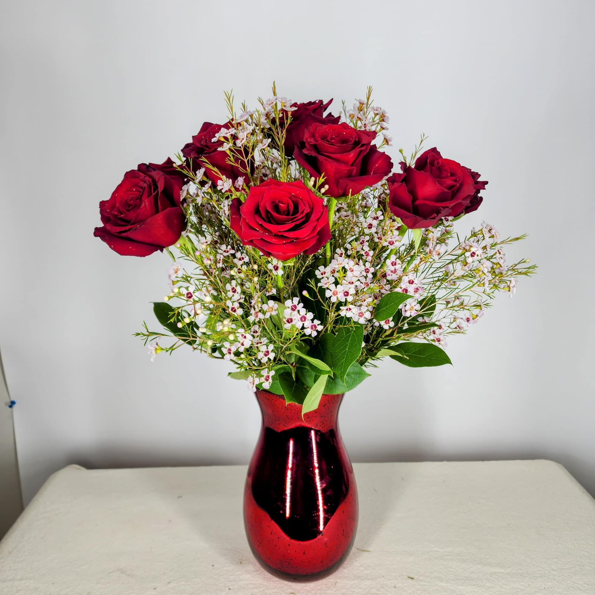 Red roses in a red glass vase with small white filler flowers