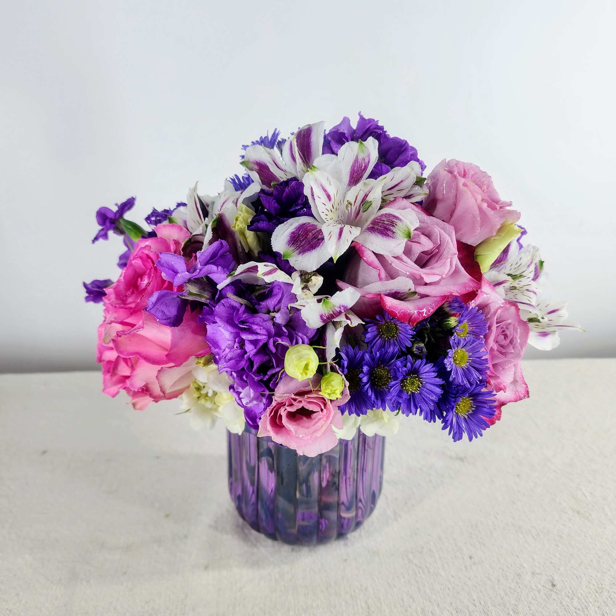 Pink and purple mixed bouquet in a purple glass vase
