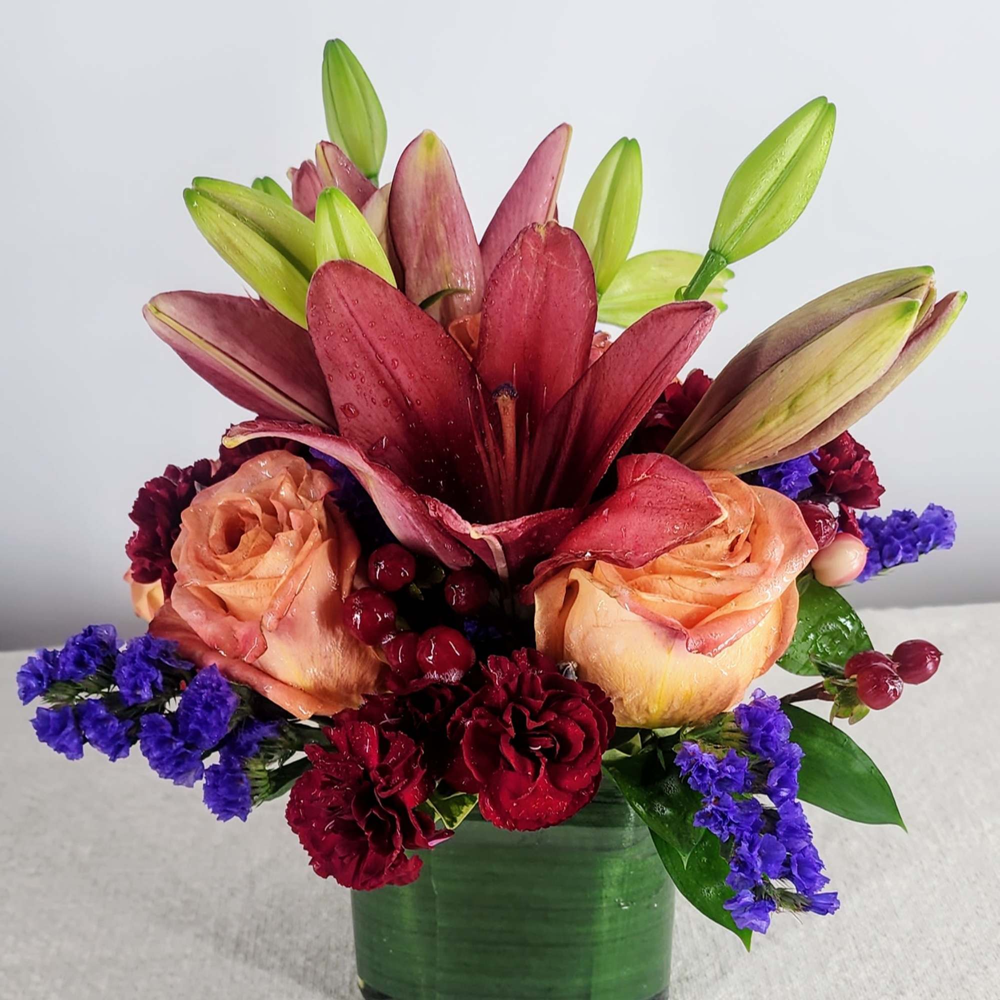Red lilies and peach roses in a green glass vase
