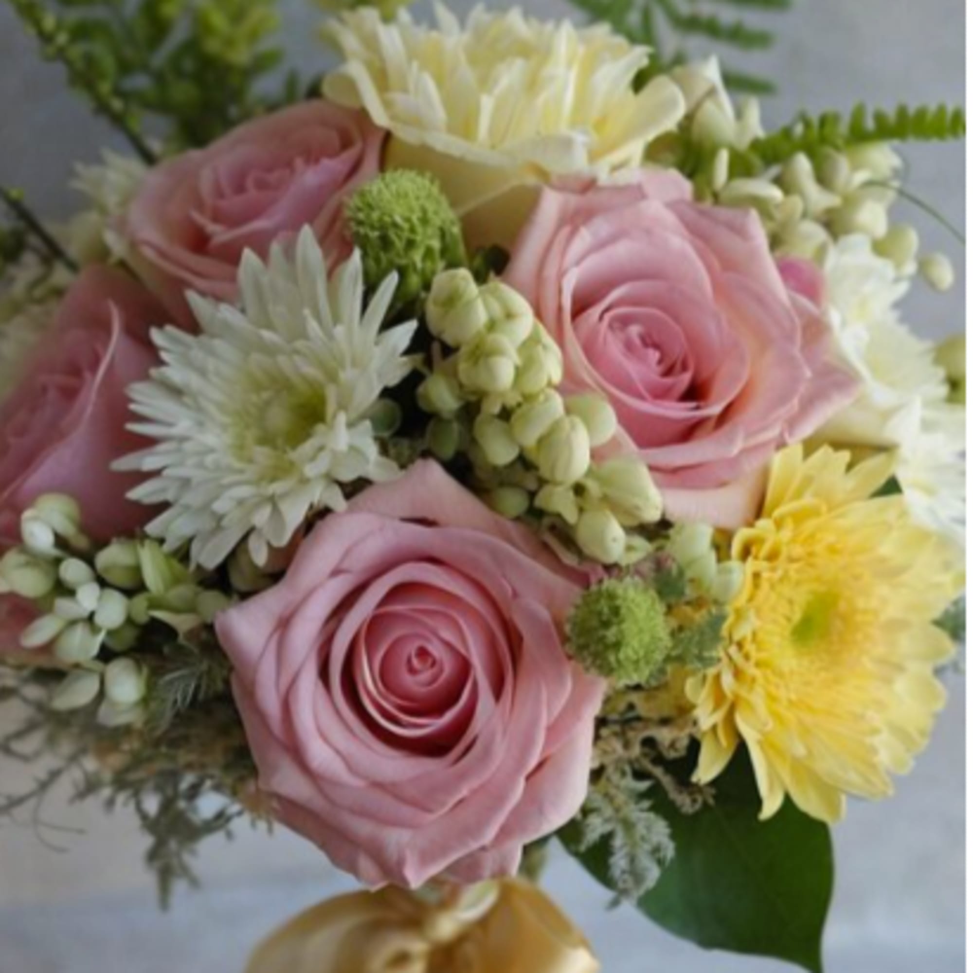 Pink roses and yellow-white flowers in a hand-tied bouquet with a ribbon