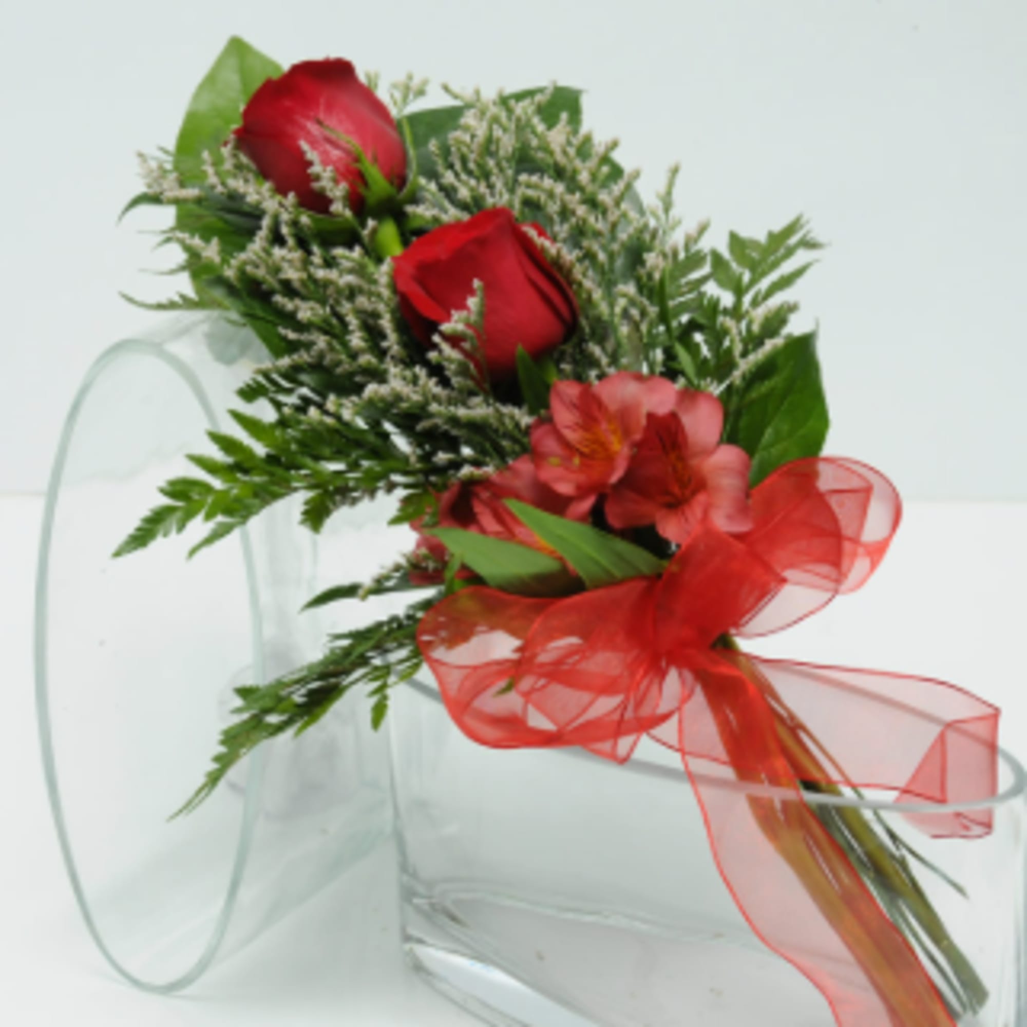 Red roses and pink flowers in a clear glass vase with a red ribbon