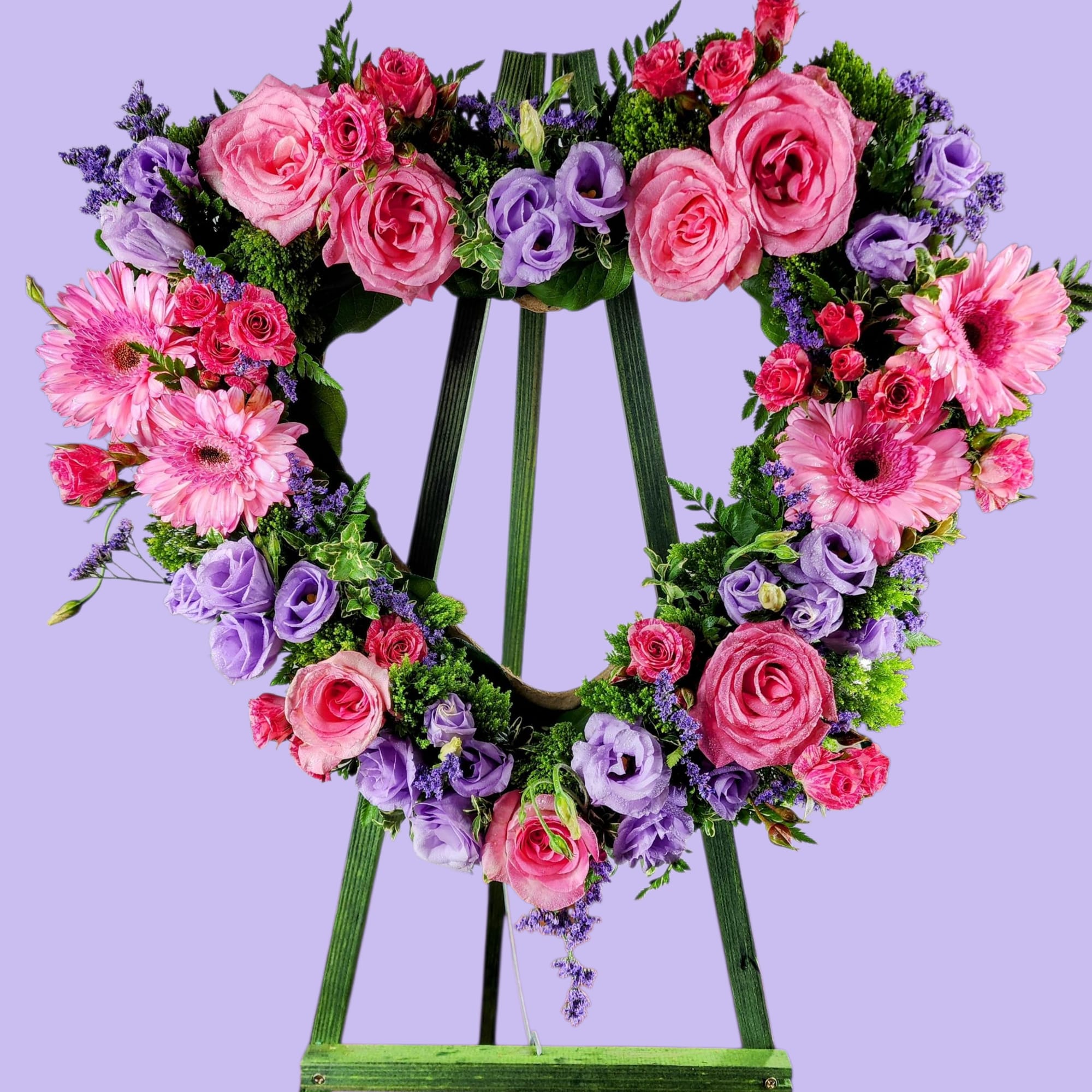 Heart-shaped floral wreath on a green easel with pink and purple flowers