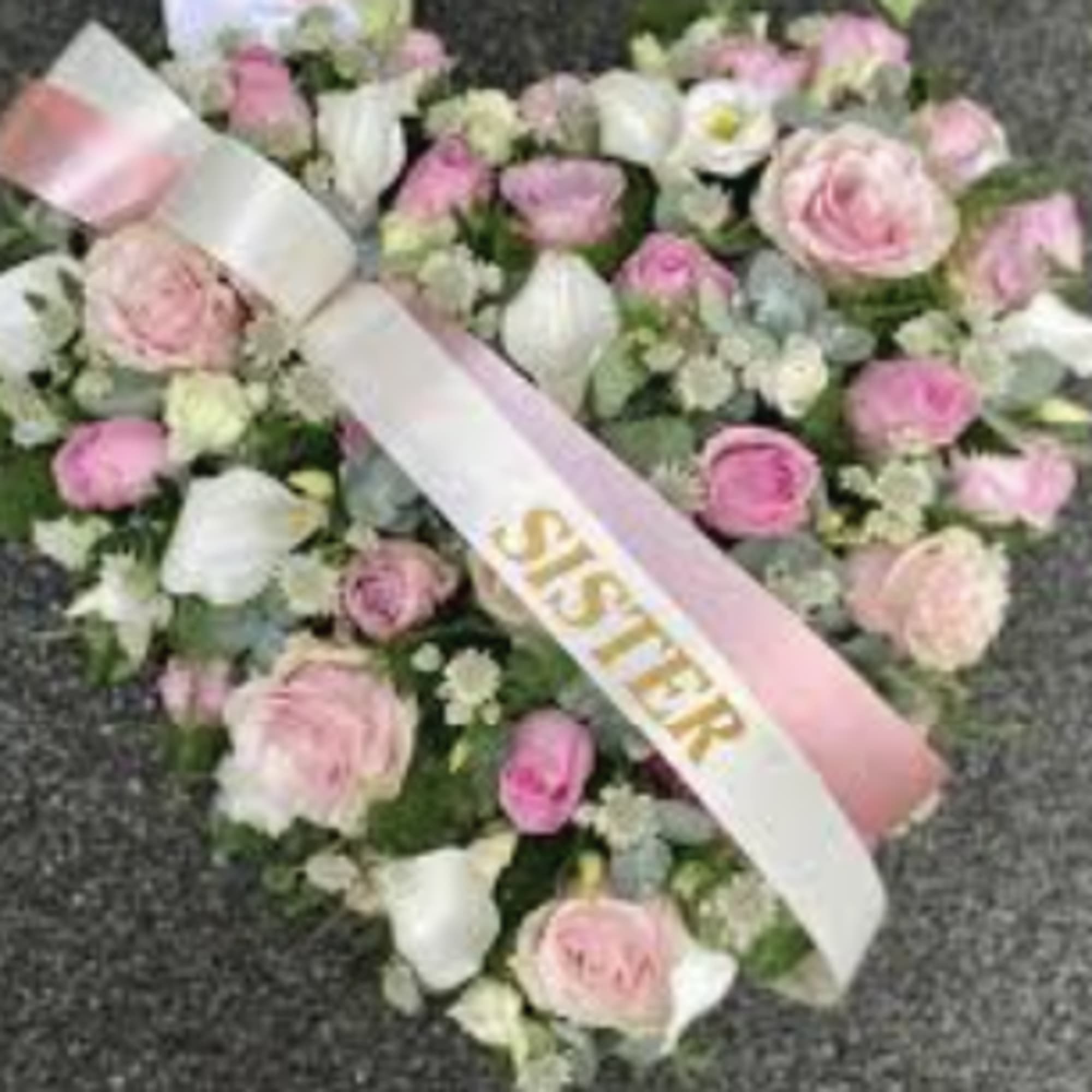 Heart-shaped pink and white floral arrangement with a sister ribbon