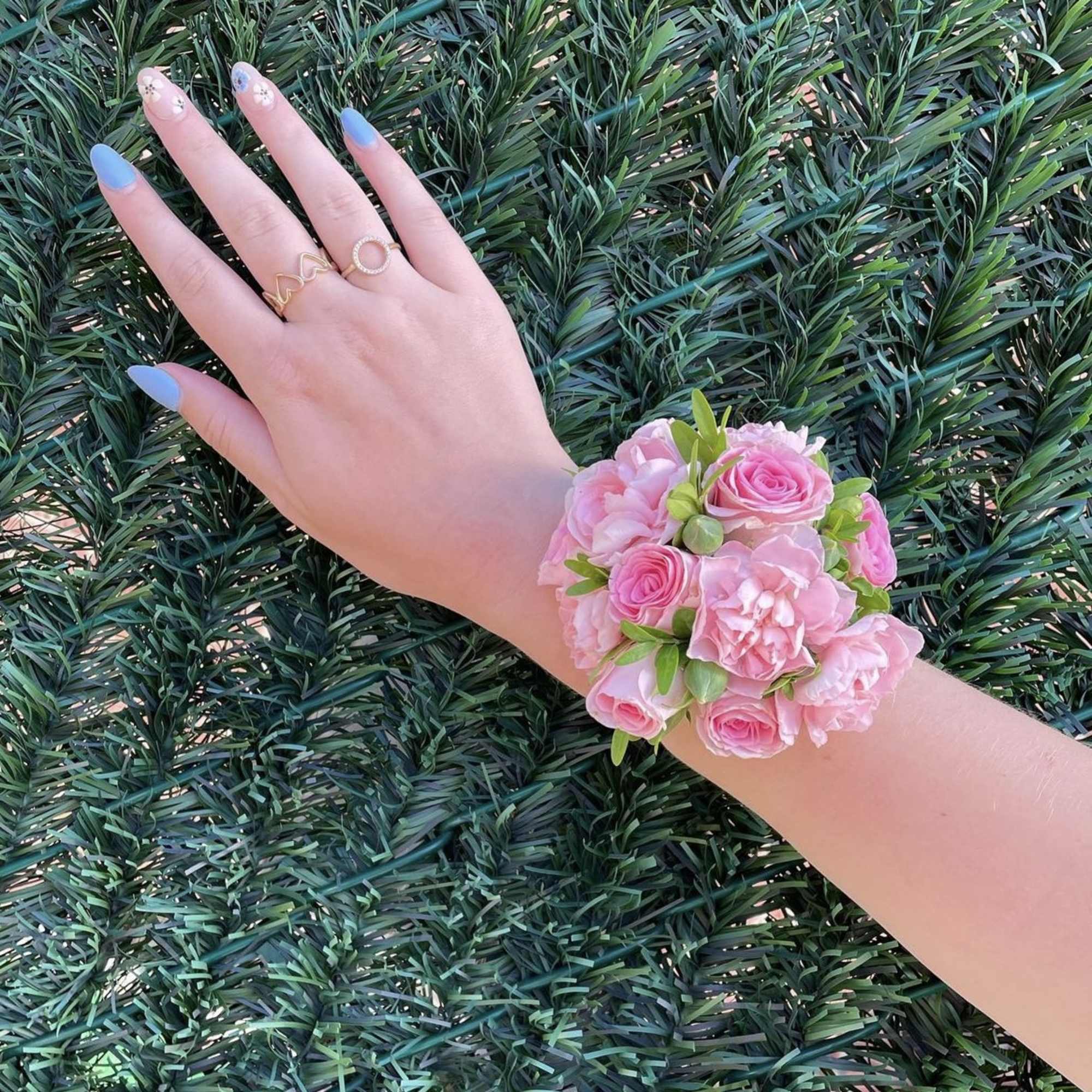 Pink floral wrist corsage on a hand with blue nails