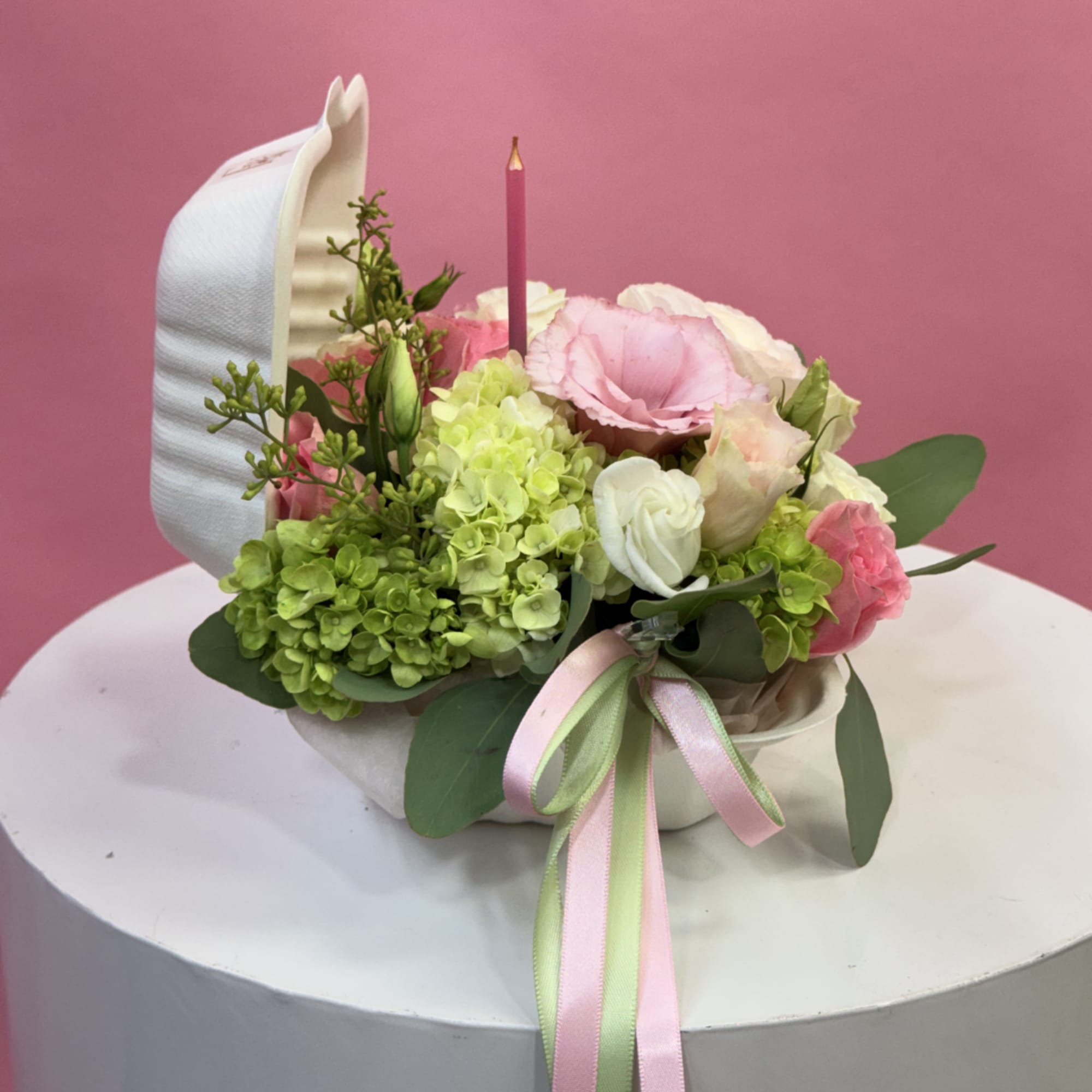 Pink and white floral arrangement with a candle in a white container