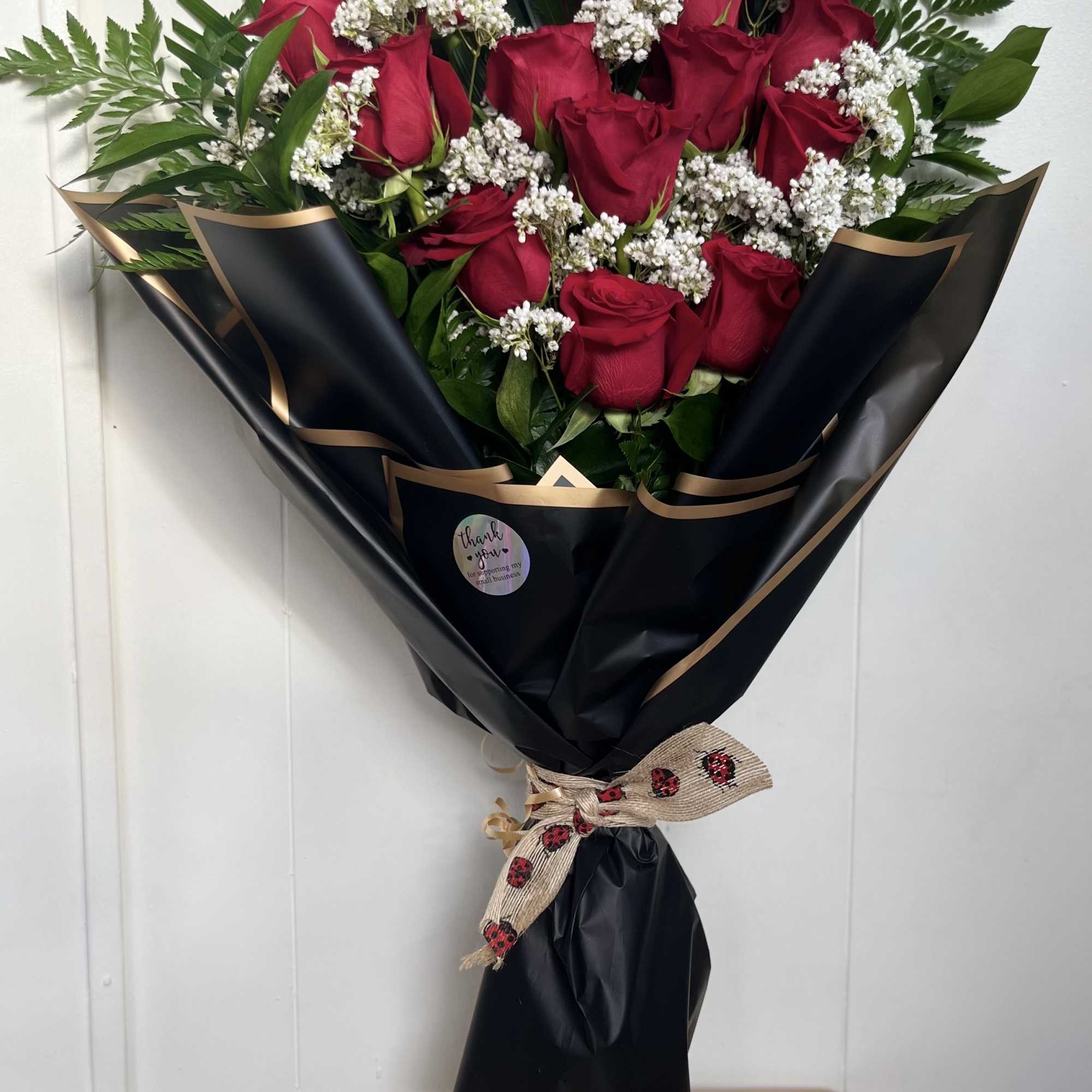 Bouquet of red roses with white filler flowers wrapped in black paper