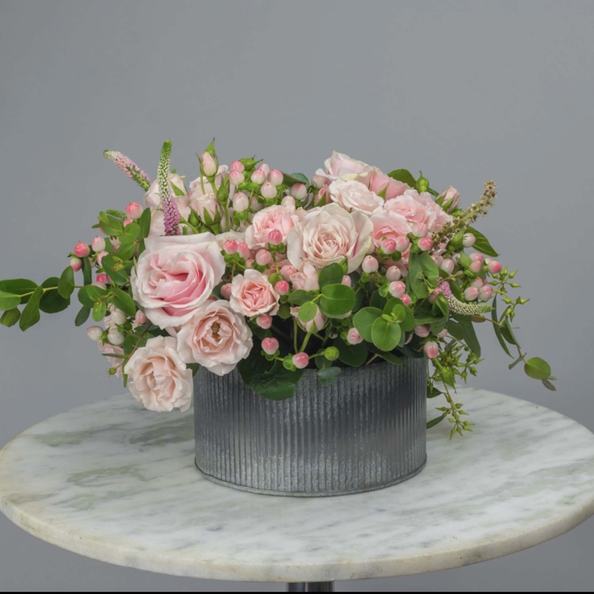 Pink roses and small blossoms in a gray ribbed container